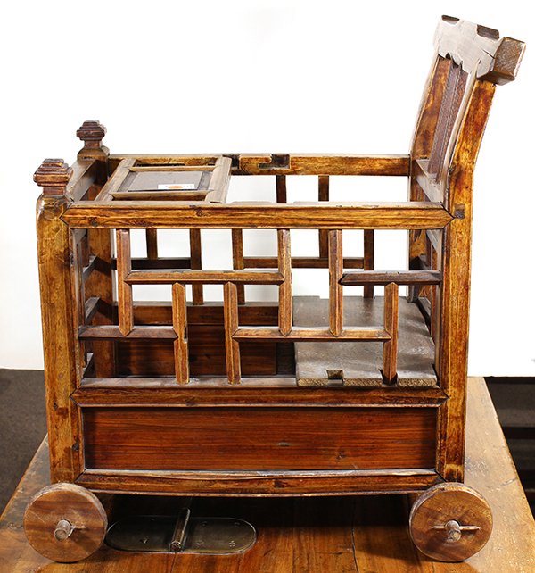 Chinese Baby Carriage: Chinese wooden baby carriage, the back with a shaped top rail and the sides with an openwork lattice pattern, with a hinged panel to confine the child, the bottom fitted with four wheels, 24.5"h x 18.
