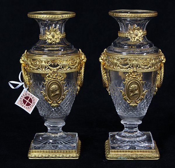 Pair of Louis XVI style French gilt bronze mounted: Pair of Louis XVI style French gilt bronze mounted urns, executed in the bacchanalian taste, each having a shouldered form with figural mounts conjoined with garland swags, surrounding the cut crystal