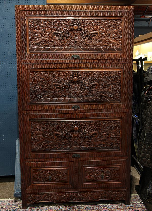 Chinese Hardwood Dragon Cabinet: Chinese hardwood cabinet, fronted by three top hinged fold out doors each carved with a pair of meandering dragons in pursuit of a jewel, above a row of two drawers having fan shaped reserves of drago