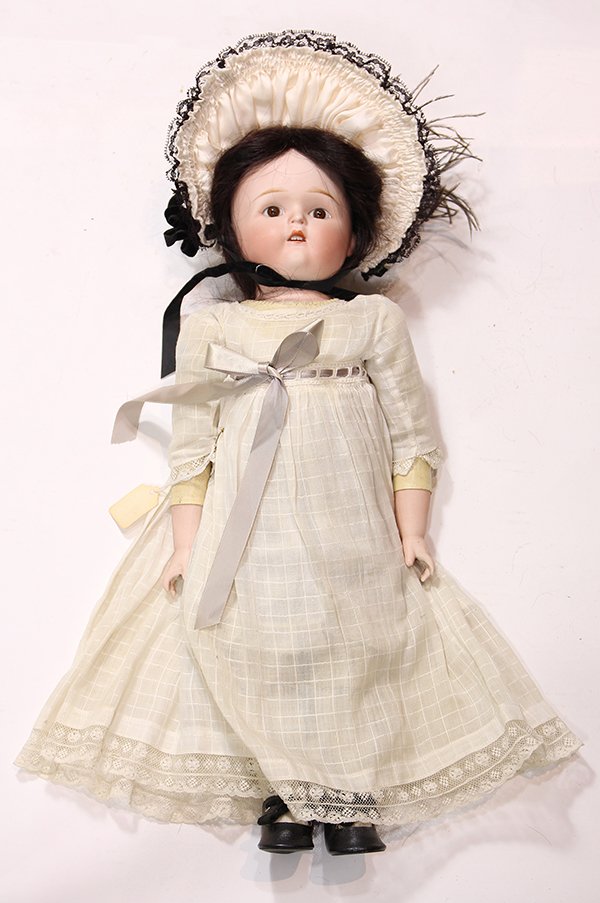 German doll: Antique bisuqe shoulder plate doll, probably Germany, the hand-decorated face set with brown stationary eyesand an open mouth with upper teeth, on a kid body wiht bisque forearms and hands, dressed ap