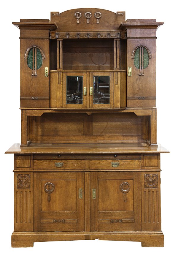 German Jugendstil buffet: German Jugendstil buffet, executed in chestnut, having a stepped cornice centering carved swags above an open shelf surmounting a cabinet with leaded glass doors, flanked by doors having oval windows 