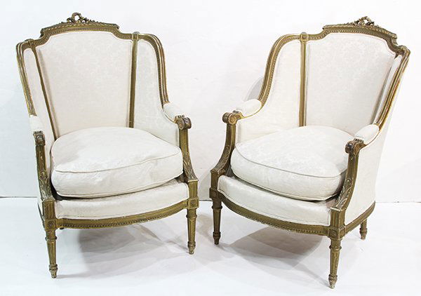 (Lot of 2) Louis XV style partial gilt bergeres: (Lot of 2) Louis XV style partial gilt bergeres, each having a ribbon crest, above a cream upholstered seat and back, and rising on fluted and tapered legs, 39"h x 26.5"w x 23"d. Provenance: Propert