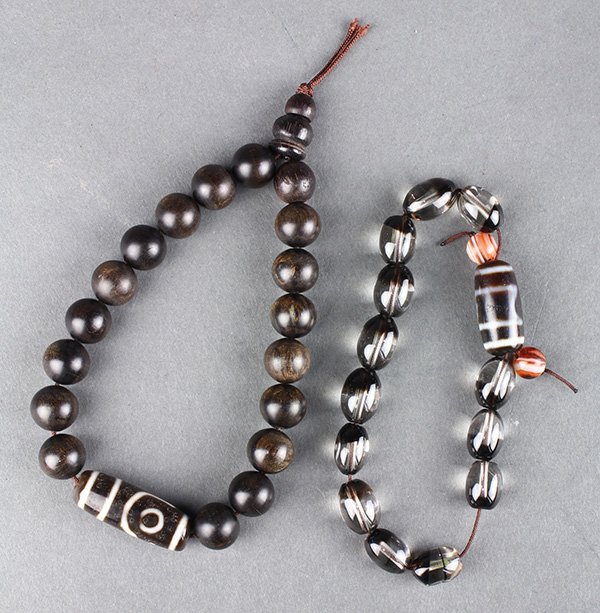 Chinese Prayer Beads, Tianzhu: (lot of 2) Chinese prayer bracelets, each with a dzi/tianzhu type bead, one consisting of an additional 13 ovoid smoky quartz beads; the other with 18 spherical wood beads, largest dzi bead: 1.25"w