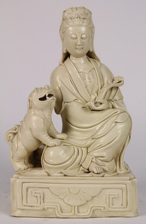 Chinese Blanc de Chinese Guanyin: Chinese blanc de chine porcelain Guanyin, seated and holding a ruyi scepter, accompanied by a fu-lion, on a rectangular plinth, the back marked 'He Chaozong', 13.5