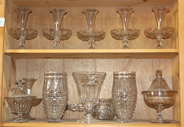 Two shelves of glassware: Two shelves of glassware, including clear glass epergnes, each having a trumpet form, above a scalloped lower tier, and rising on a conforming base, 8.5"h