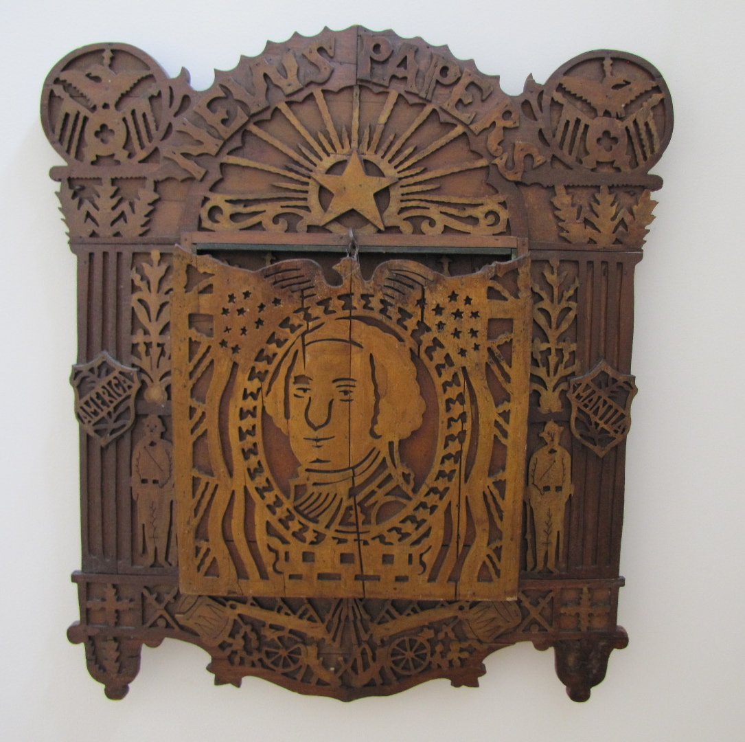 Scroll Saw Fretwork Newspaper Holder: Scroll saw fretwork George Washington/Spanish American newspaper holder with eagles, flags, drums, cannons, stars and leaf applied decorations. Some remaining old gold paint; 22 3/4"H, 21 1/4" W. Some