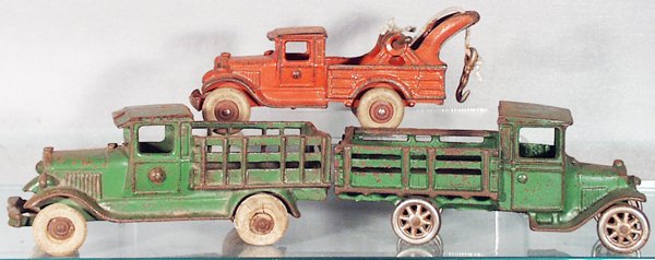 3 CAST IRON TRUCKS: painted cast iron, AC Williams Wrecker, 7 in long, white rubber tires, replaced tow rope; AC Williams Stake Truck, 7 in long, white rubber tires rough; Arcade Stake Truck, nickel wheels, 7 in long, al