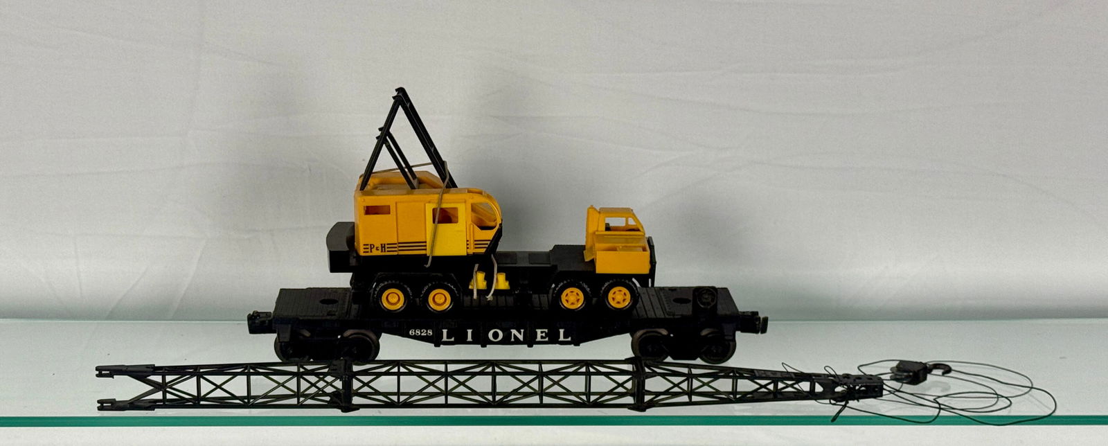 Lionel 6828 Mobile P&H Construction Crane Car: A Lionel 6828 Postwar P&H Crane Car, comprising a black vintage model train flatcar prominently displaying "LIONEL" and the number "6525" in white text on its side. The flatcar carries a disassemb