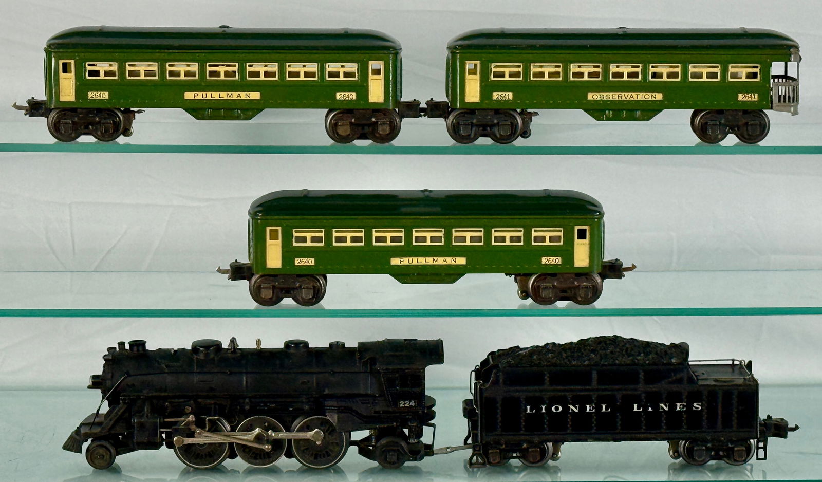 Lionel O-Gauge Passenger Set: The black locomotive is marked "224" and the black 2224T tender The three passenger cars are dark green with cream/yellow trim around windows and door sections. Two of these cars are marked "PULLMAN 2