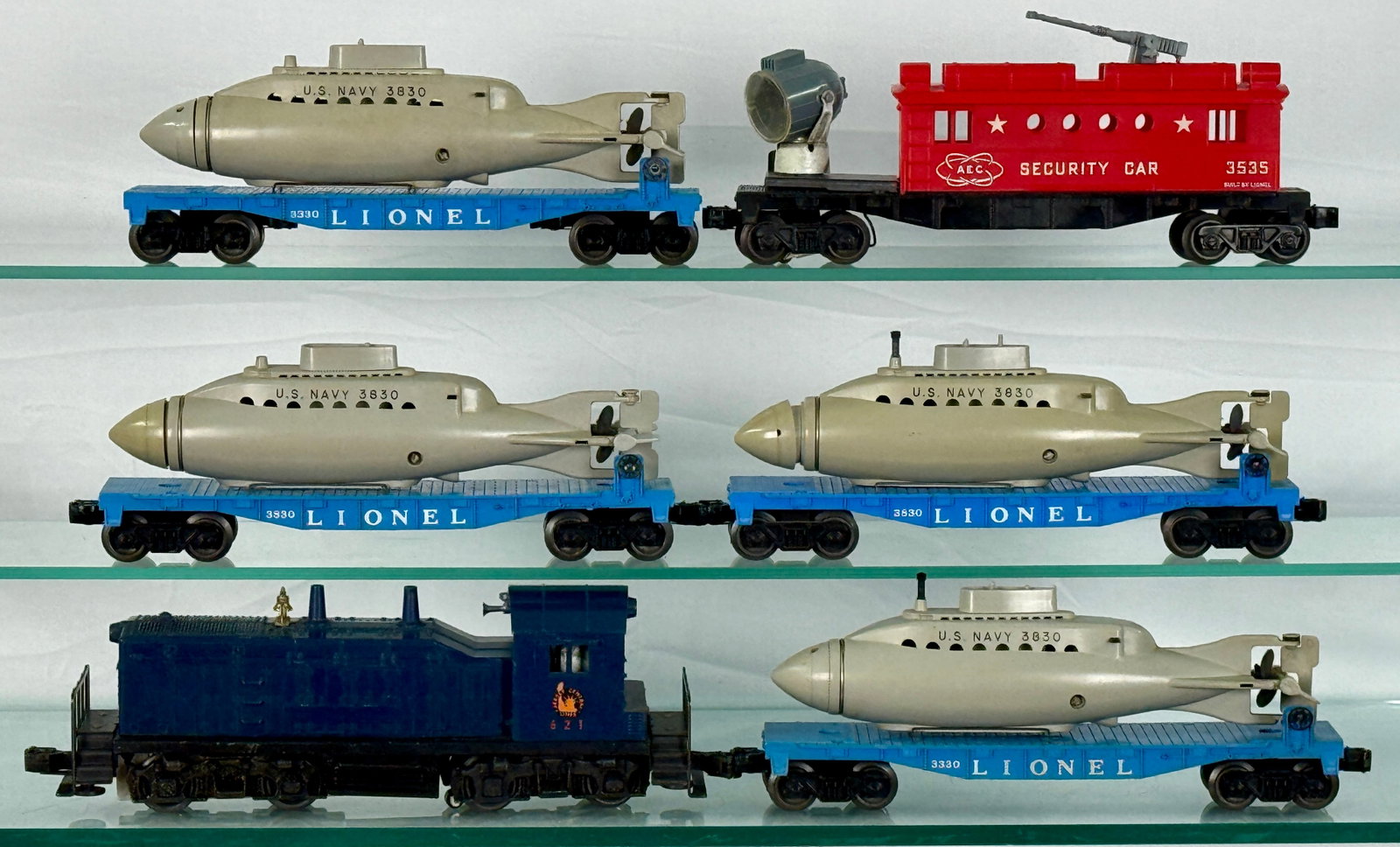 Lionel O Gauge Submarine Train Set: A blue 621 Jersey Central diesel-style locomotive. The lot comprises two 3330 and two 3830 blue flat cars, each carrying a gray U.S. Navy 3830 submarine. Also included is one Lionel 3535 'A.E.C. SECUR