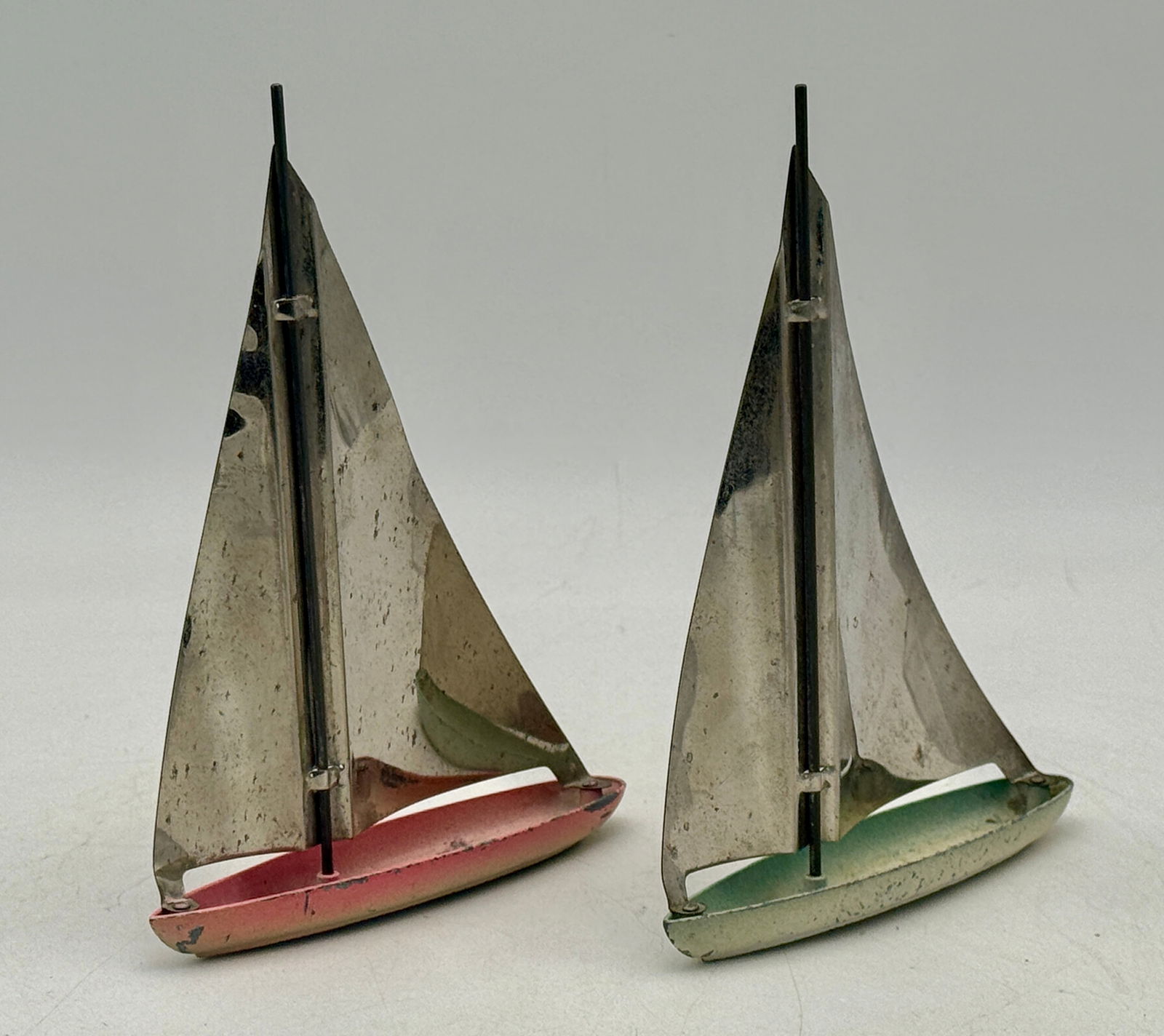 A Pair of Tootsietoy 1015 Art Deco Style Metal Toy Sailboats: A pair of Art Deco style metal toy sailboats, one with a red hull and the other with a light green hull, both featuring silver/metallic sails and masts 5 x 6 3/4 inches, circa 1937, C7.