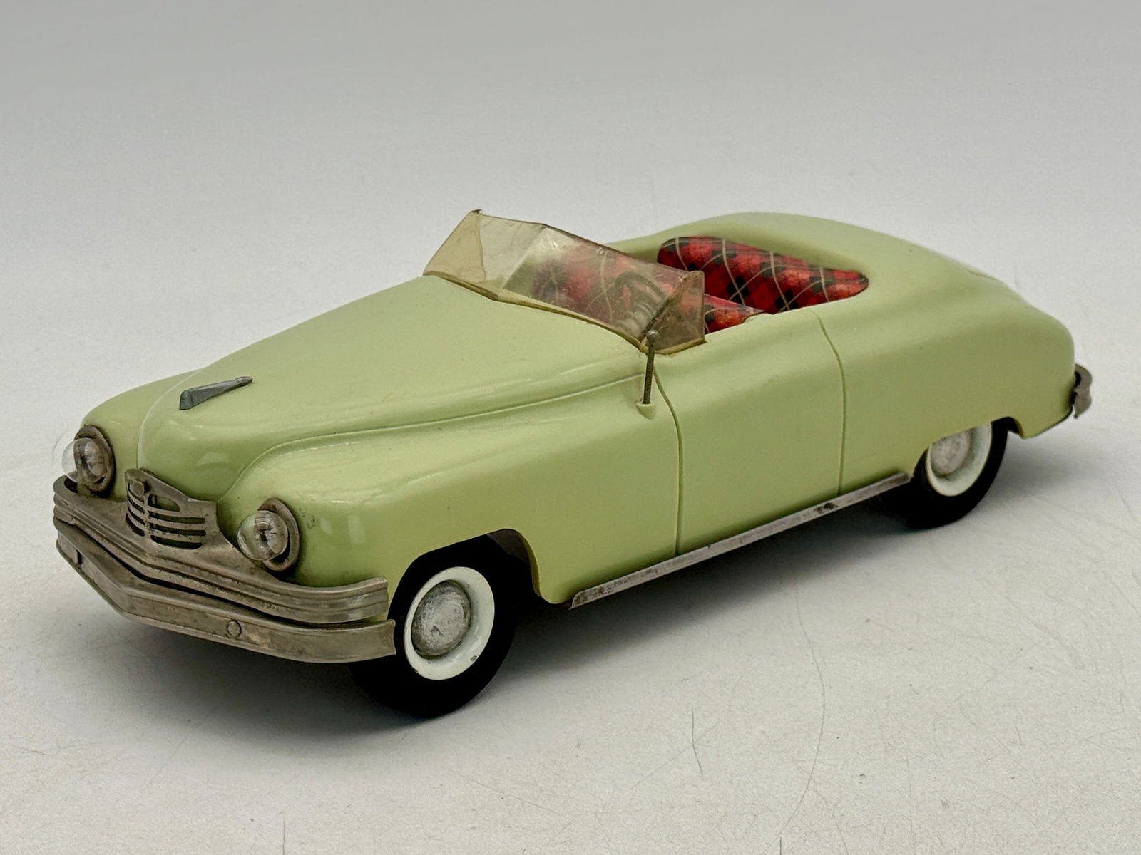 1950s Conway Packard Wind-Up Convertible Toy Car: A single light green Conway Packard working wind-up convertible toy car with a red and white plaid interior, featuring a silver-colored grille and bumpers, plastic, 12 inches , body has minor warp, C8