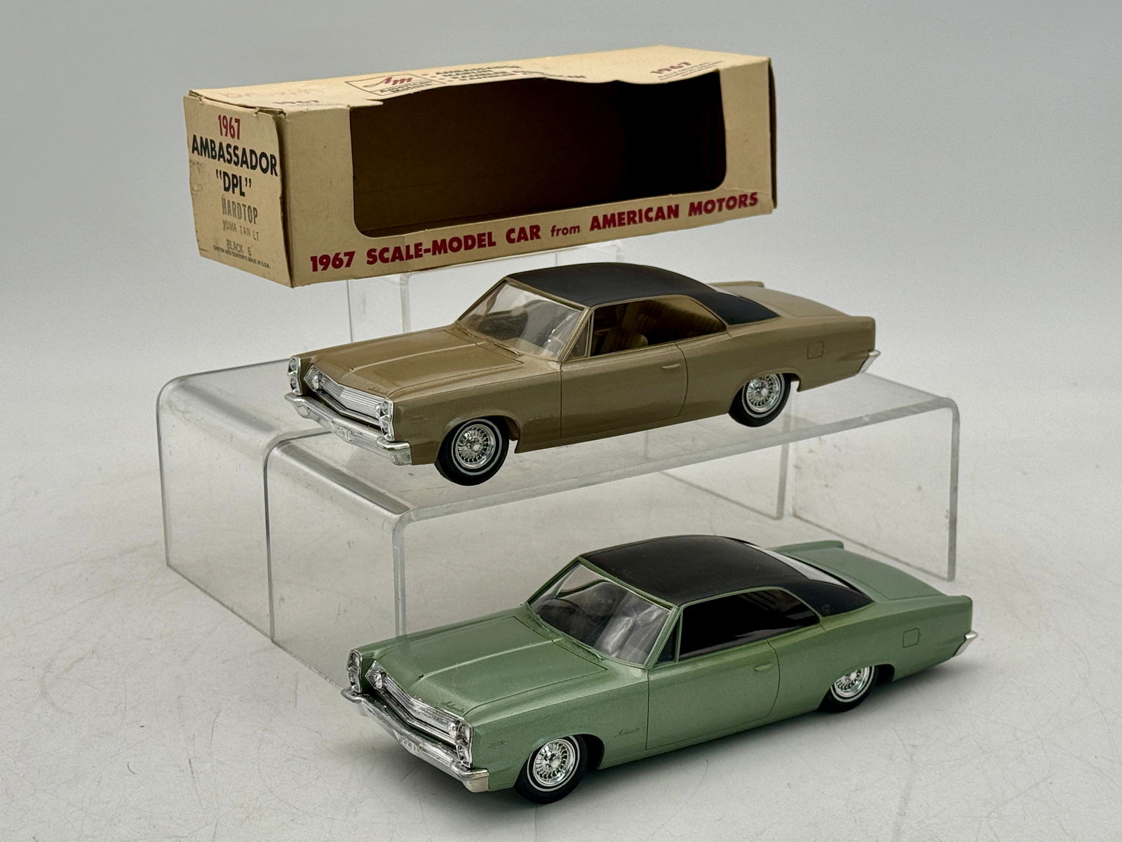 Two Jo-Han 1967 American Motors Ambassador DPL Hardtop Promo Models: Two 1967 Ambassador "DPL" Hardtop scale model cars, one Laurel Green with a black roof Radio Version, and one metallic tan with a black roof, accompanied by a cardboard box labeled "AM 1967 AMBASSADOR