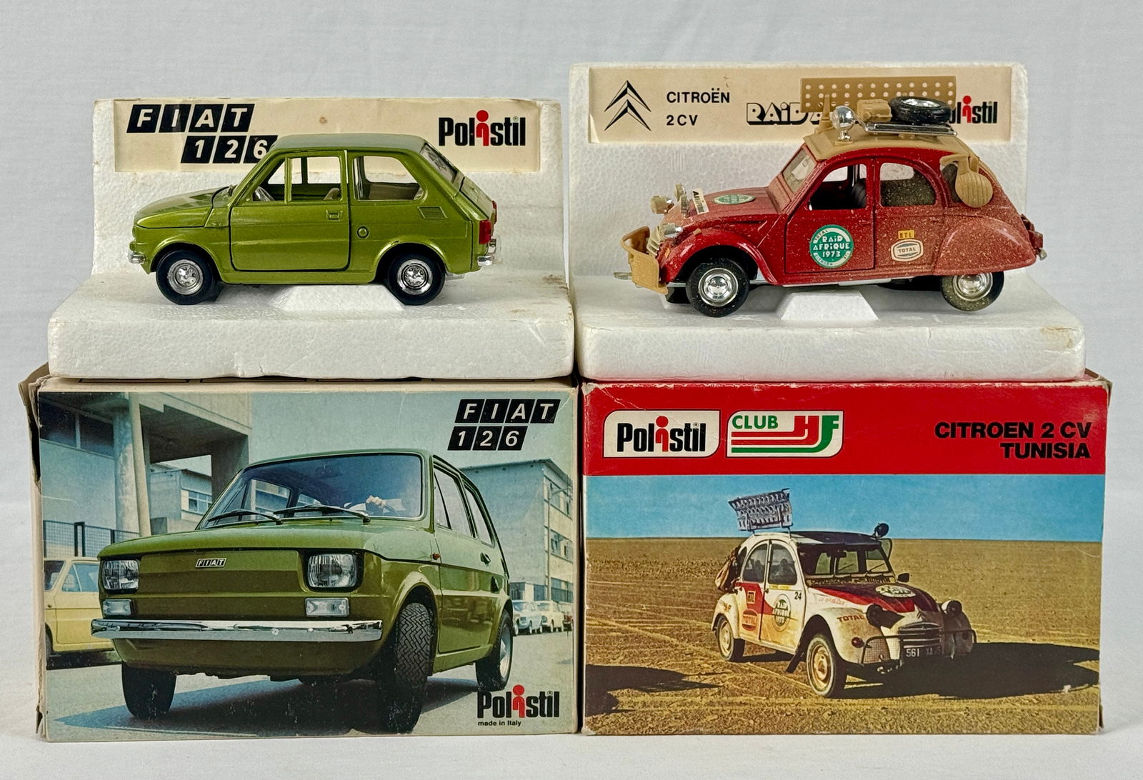 A Pair of Polistil Die-Cast Model Cars: A pair of Polistil die-cast model cars, including a red Citroen 2CV "RAID AFRIQUE" with "TOTAL" branding and a green Fiat 126, each displayed on a labeled stand and accompanied by its original box C9.