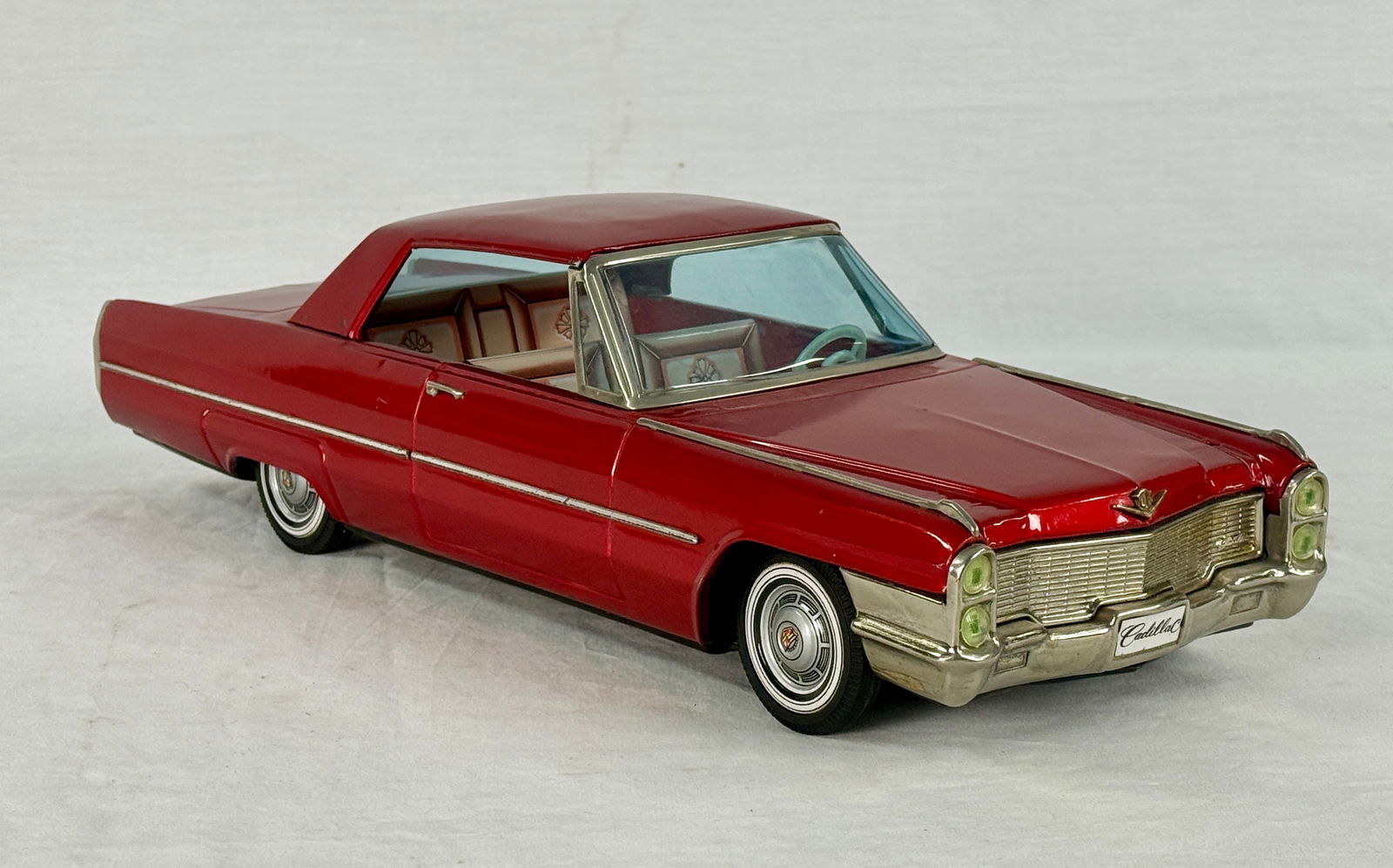 ATC Red 1965 Cadillac DeVille Toy Car: A red 1965 Cadillac DeVille toy car with chrome accents, blue windows, a cream interior, and "Cadillac" script on the front grille and rear bumperLitho Tin 16.5 inches friction working, C8.