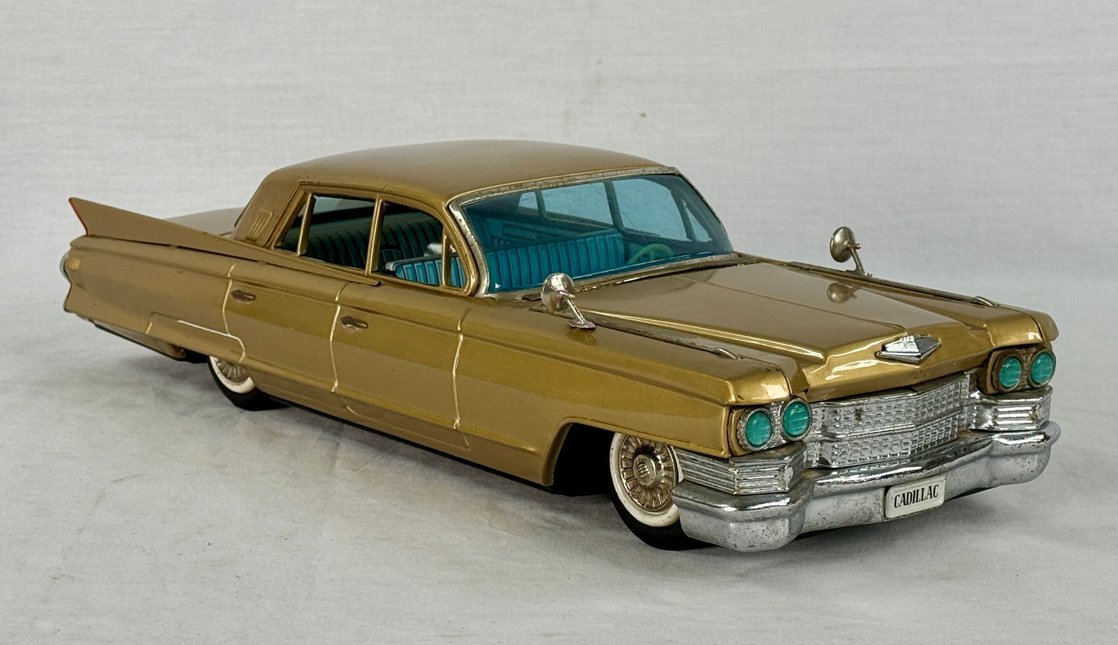 Large Bandai 1961 Japanese Tin Friction Cadillac Toy Car: A large 17 inch Bandai 1961 Japanese tin litho friction toy car, a gold-colored model Cadillac with blue windows and interior, featuring "CADILLAC" text on the license plates with working fricti