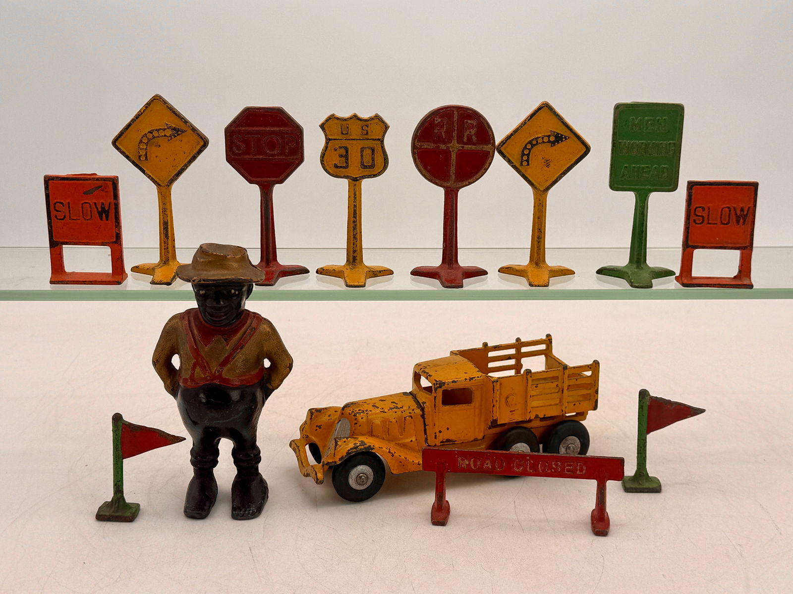 A Collection of Arcade Cast Iron Road Signs, Bank, and Toys: Eleven Arcade cast iron road signs in yellow, red, orange, and green, displaying text such as "SLOW", "STOP", "U.S. 30", "R.R. CROSSING", and "MEN WORKING AHEAD", AC Williams Share Cropper Still Bank,