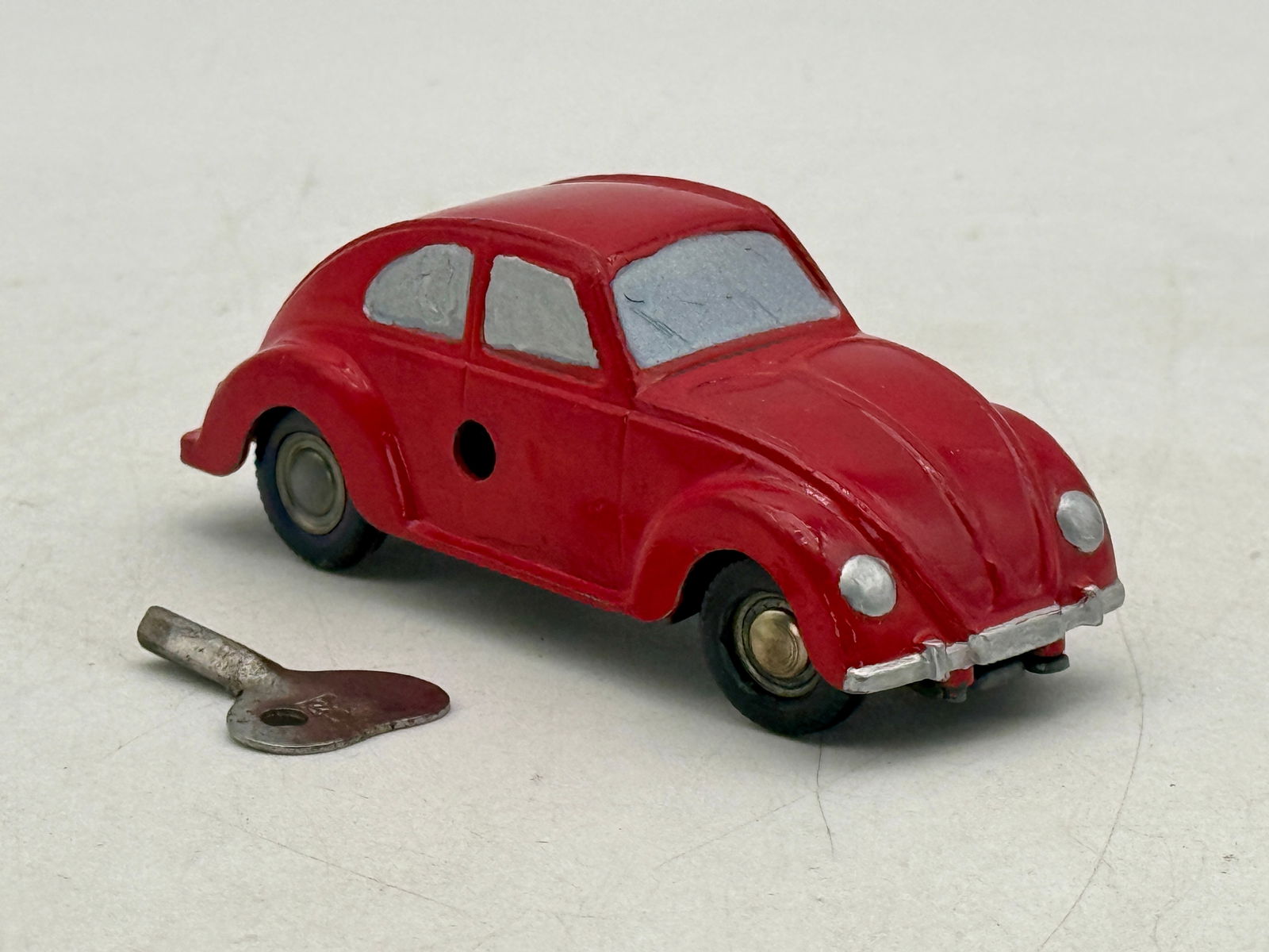 Prameta Red Volkswagen Beetle Wind-Up Toy Car: A red repainted wind-up working Volkswagen Split Window Beetle, with grey windows, black wheels, and a metallic winding key, marked 'MADE IN US ZONE GERMANY' on the underside, Front Steering mec
