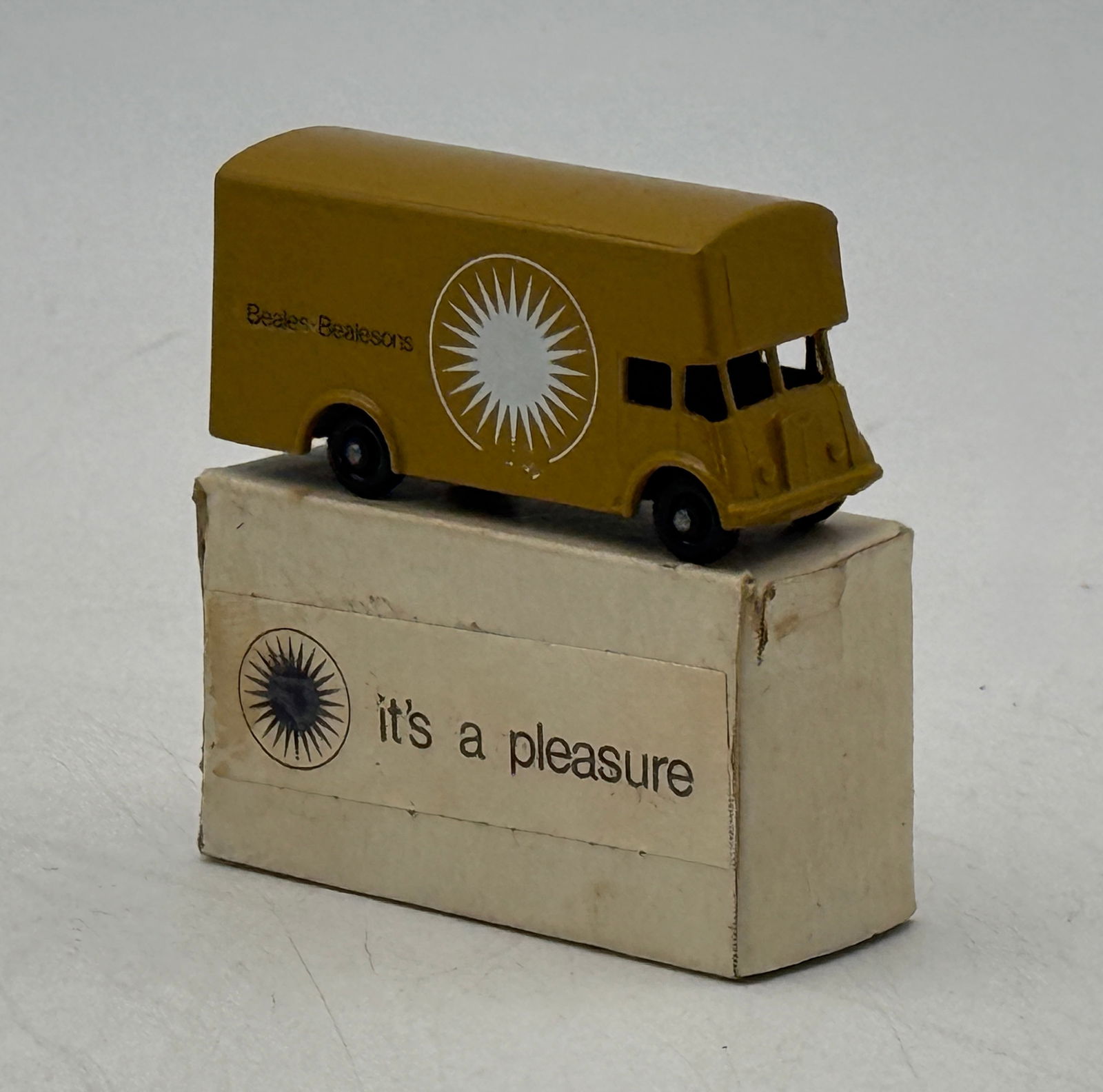 Matchbox 46B9 Beales Bealesons Toy Delivery Van with Box: St Code 21 A mustard yellow Matchbox Lesney toy delivery van, marked with a white sunburst logo and "Beales Bealesons" on its side, resting on its beige box which features a dark sunburst logo and the