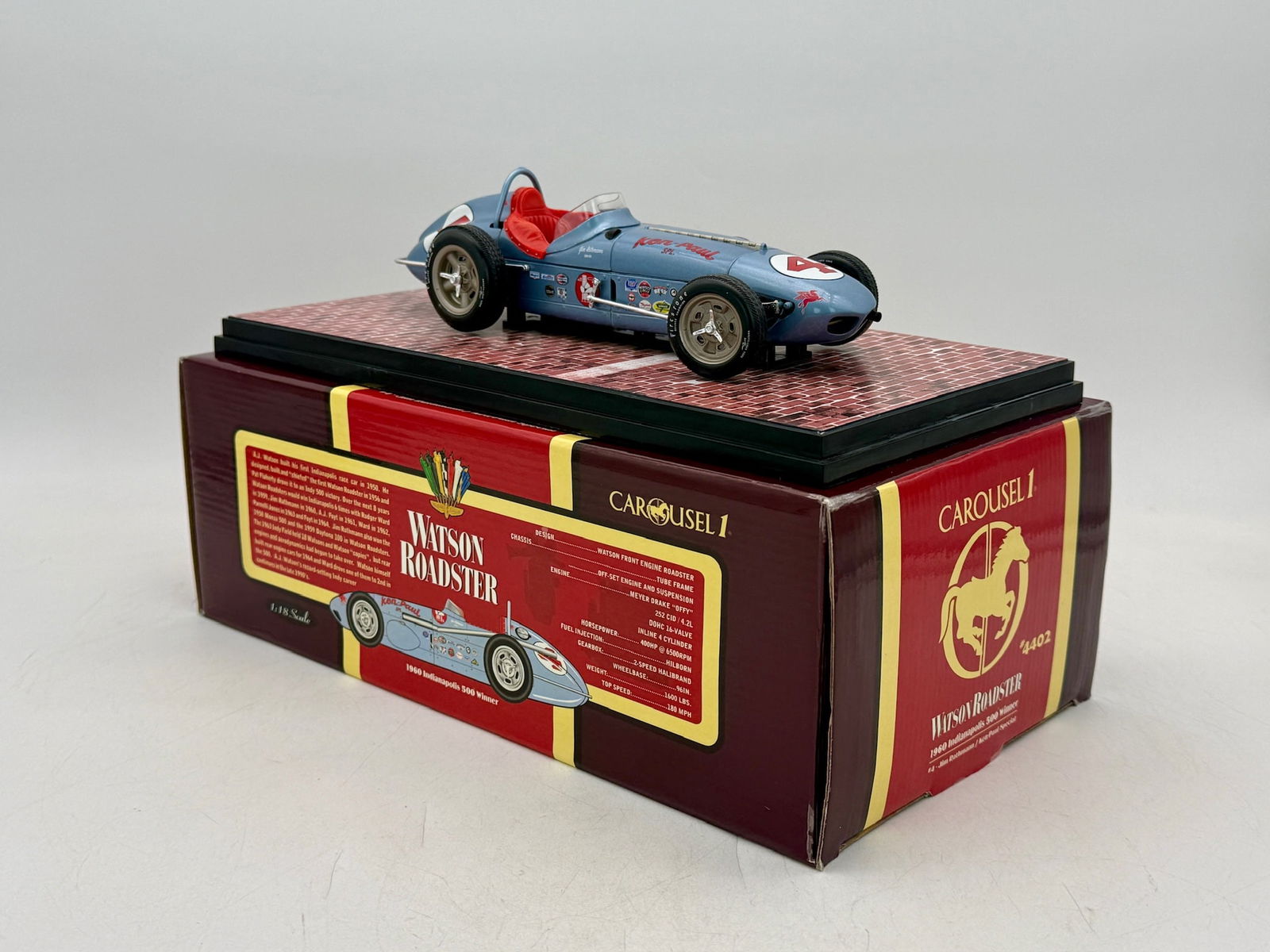 Carousel 1 1:18 Jim Rathmann 1960 Indy 500 Watson Roadster: A blue 1:18 scale die-cast model of the #4 Ken-Paul Special Watson Roadster including a brick-patterned base, certificate of authenticity, and original packaging. 9 inches long shipping box, OB and in