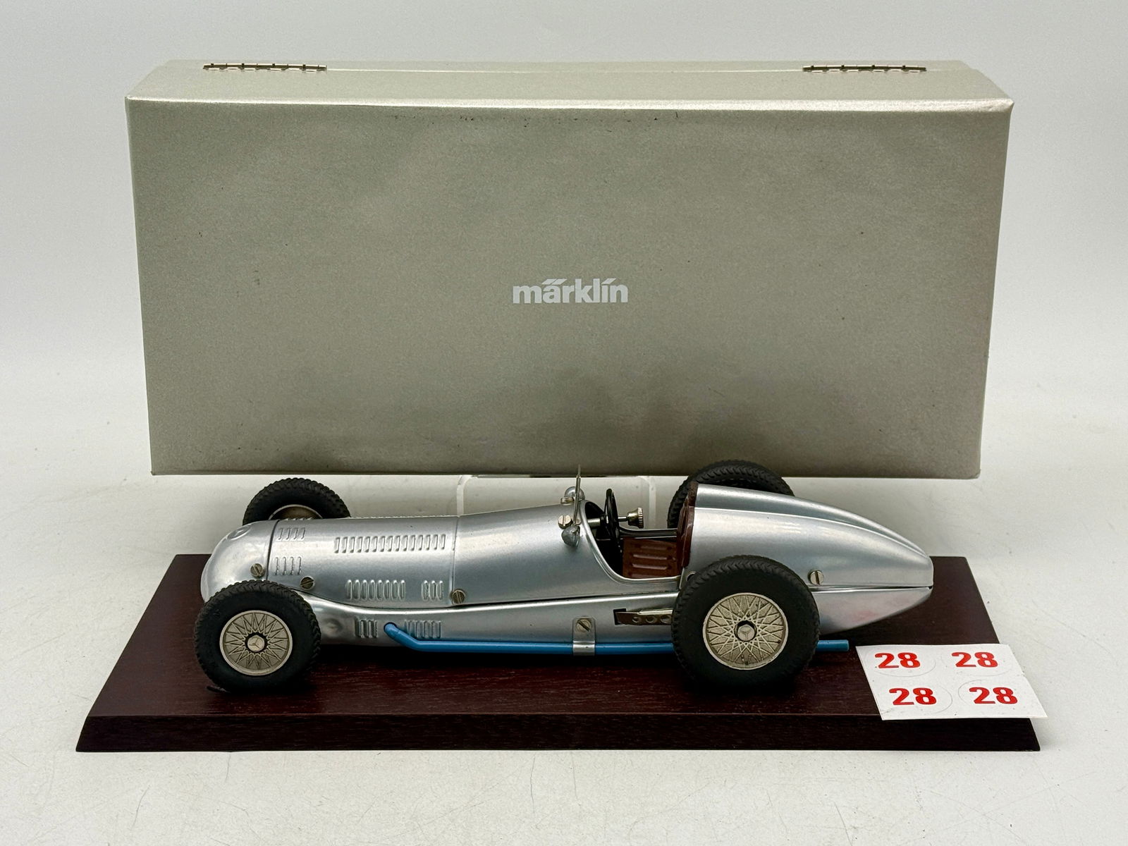 Marklin Mercedes-Benz Silver Racing Car W125: A silver Marklin model Mercedes-Benz racing car featuring a blue exhaust pipe and brown interior, mounted on a dark wood base with its original light grey hinged storage box. 10 1/2 inches long mounte