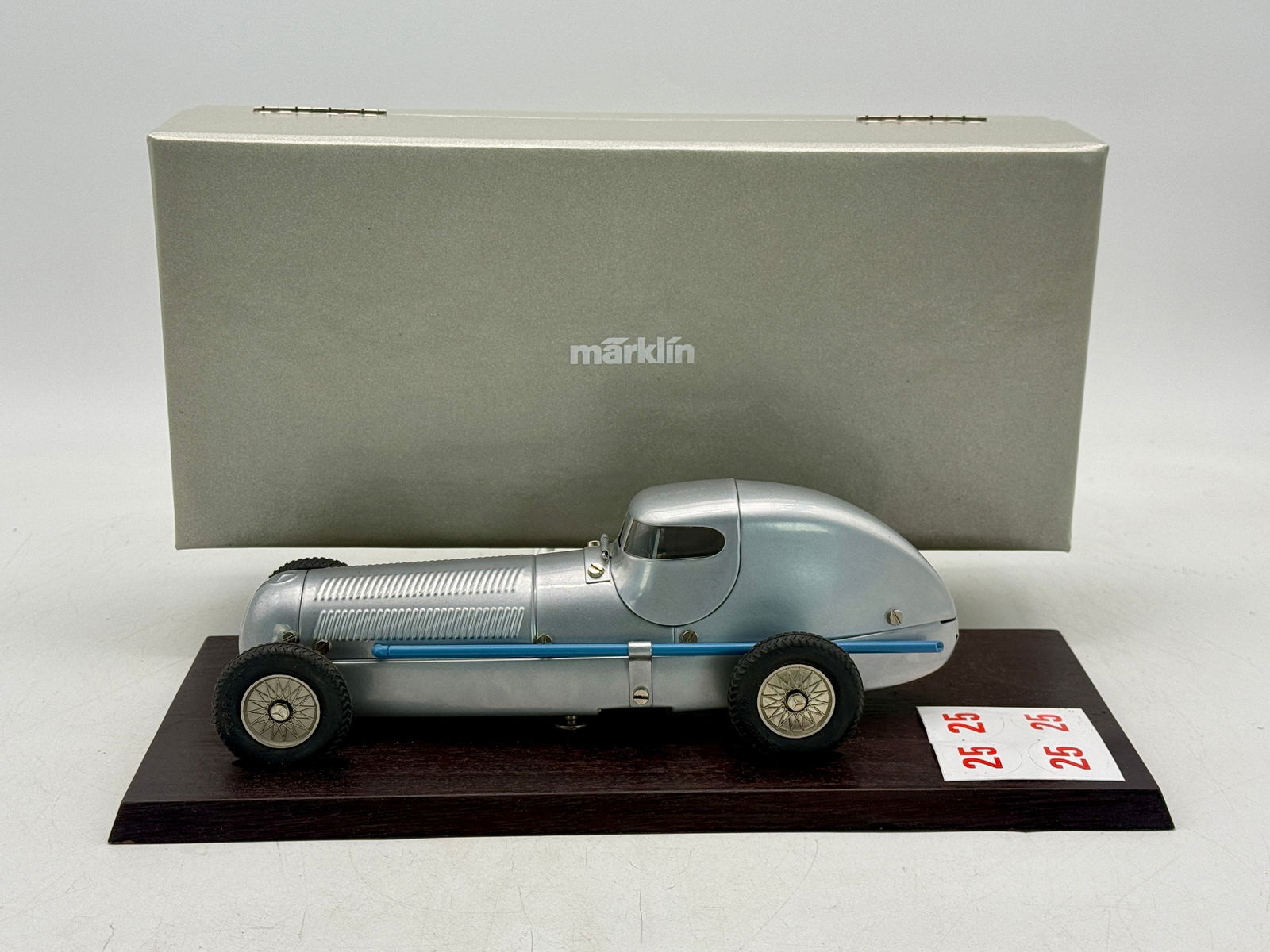 Marklin Mercedes-Benz W25 Silver Arrow Model Racing Car: A silver-colored MarklinMercedes-Benz W25 streamlined racing car accompanied by a dark wooden display base, original silver box, and red number 25 decals. Painted 10, 10 1/2 inches long CW/W, W/key OB
