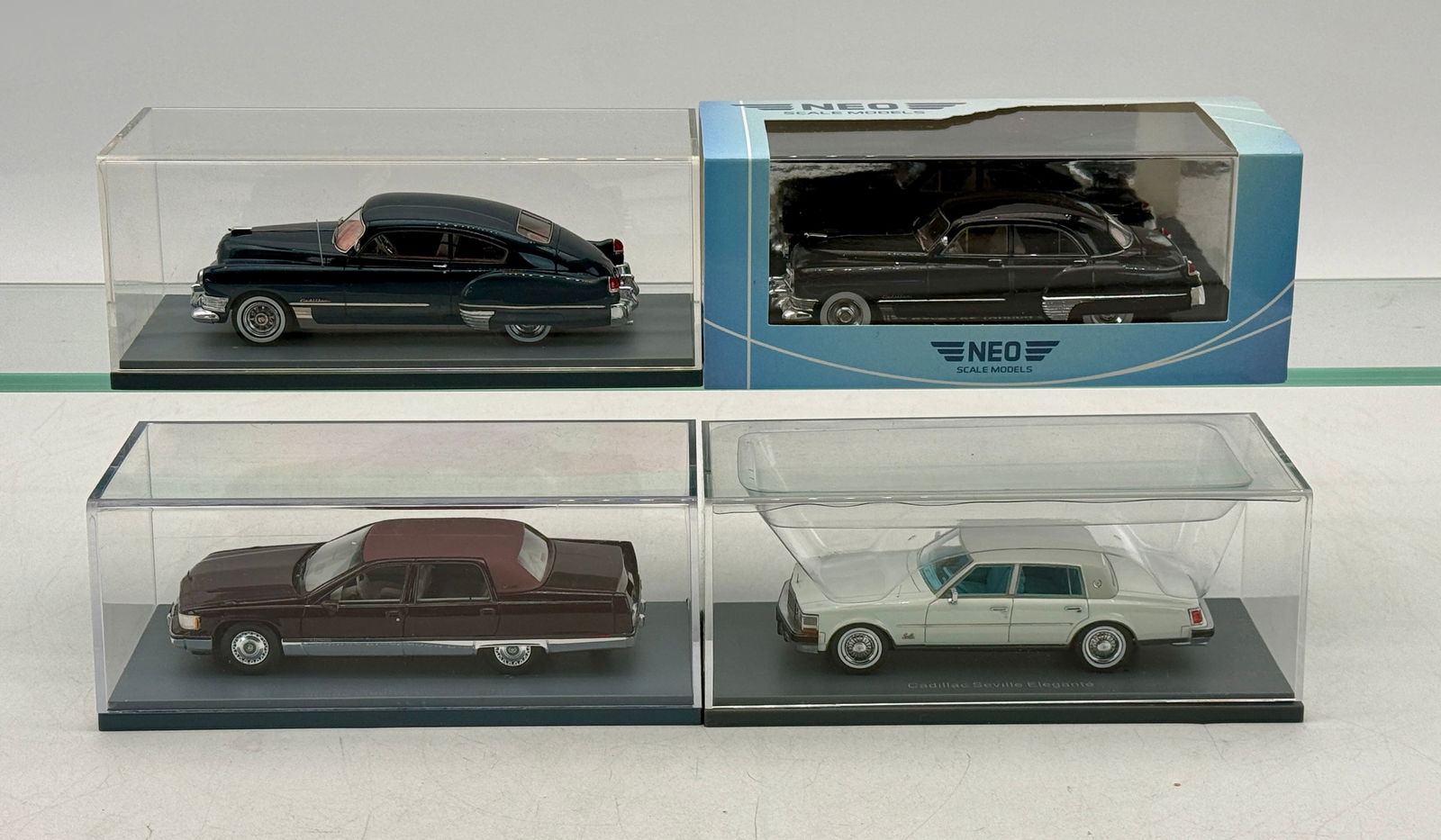 4 NEO Scale Models 1:43 Cadillac Model Cars: A collection of 1:43 scale resin model cars including Cadillac Series 62 Touring Sedans and a Cadillac Seville Elegante in dark blue, black, maroon, and white, each presented in a clear display case.