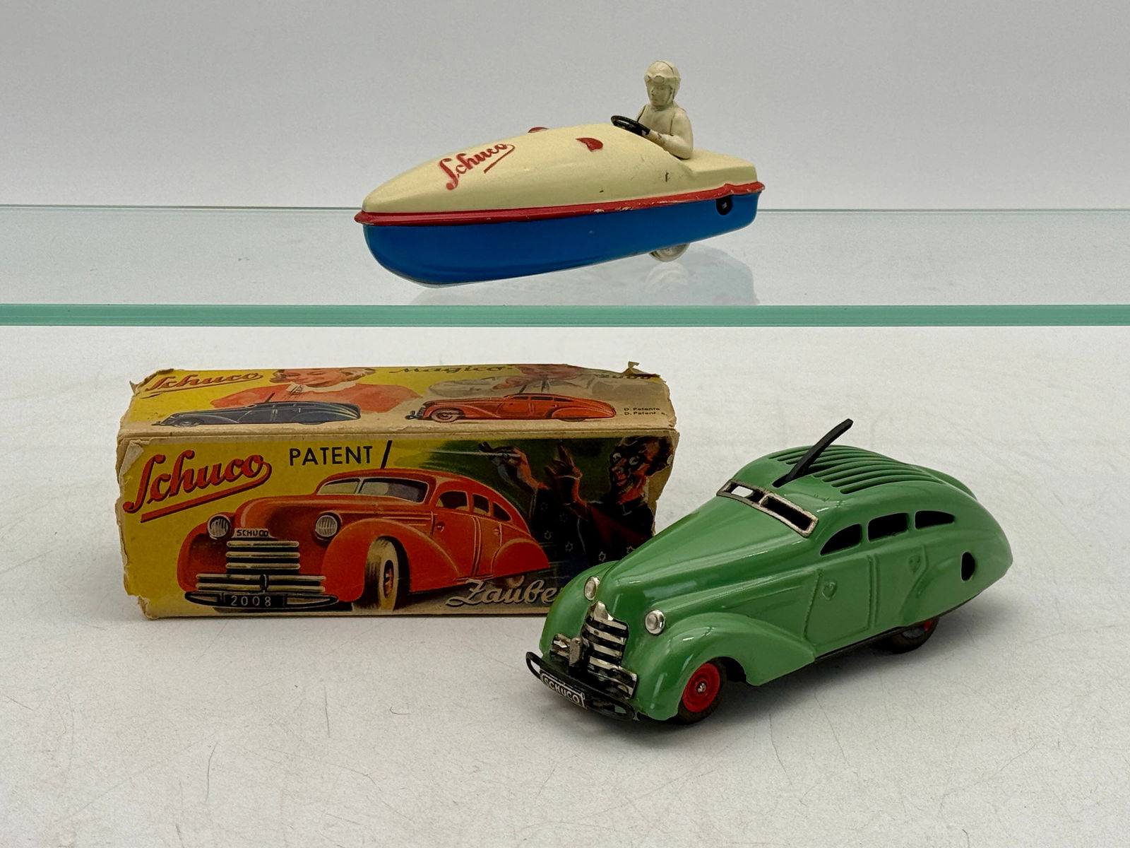 Two Schuco Vintage Tin Wind Up Toys: A green Schuco Magico-Auto 2008 with original box and a cream and blue 1015 boat with driver, both are working with one worn original box, C7-8.
