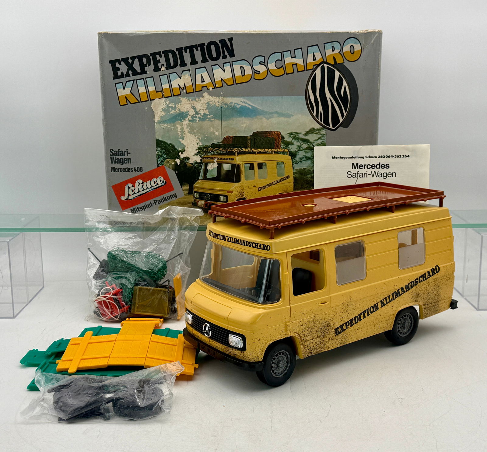 Schuco Mercedes Benz 408 Safari-Wagen Expedition Kilimandscharo Toy Set: A collection of Schuco toy components featuring a yellow Mercedes 408 Safari-Wagon with its original box, assembly instructions, and assorted accessories and parts, C9.