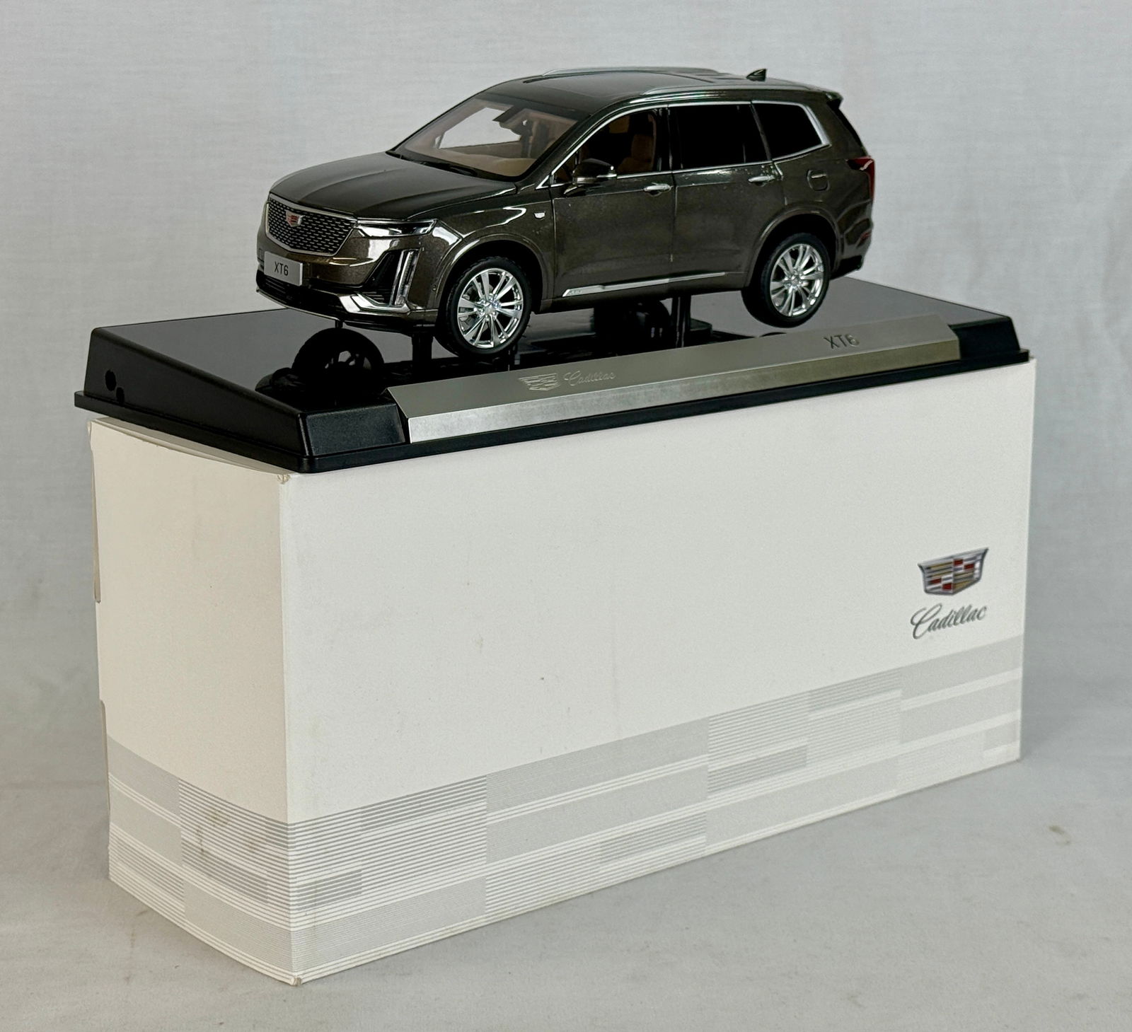 Cadillac XT6 Dealer Promo: A 1:18 scale resin/diecast model of a Cadillac XT6 SUV featuring a dark metallic Scorpion Met finish, mounted on a branded display base and accompanied by its original packaging. 11" long, OB C9.