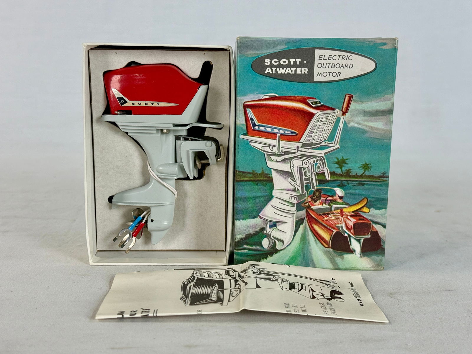 Scott-Atwater Fleet Line Miniature Electric Outboard Motor with Box: A vintage red and light gray #36 Scott-Atwater Fleet Line miniature electric outboard motor with its original decorative box and an instruction sheet marked Japan, C10.