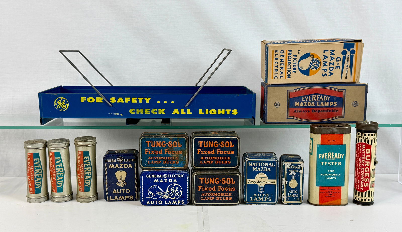 A Collection of Vintage Automotive Lamp Bulb Packaging and Accessories: A collection of vintage automotive lamp bulb tins and cardboard boxes from brands including General Electric Mazda, Tung-Sol, and Eveready, accompanied by a GE metal display tray, an Eveready tester,