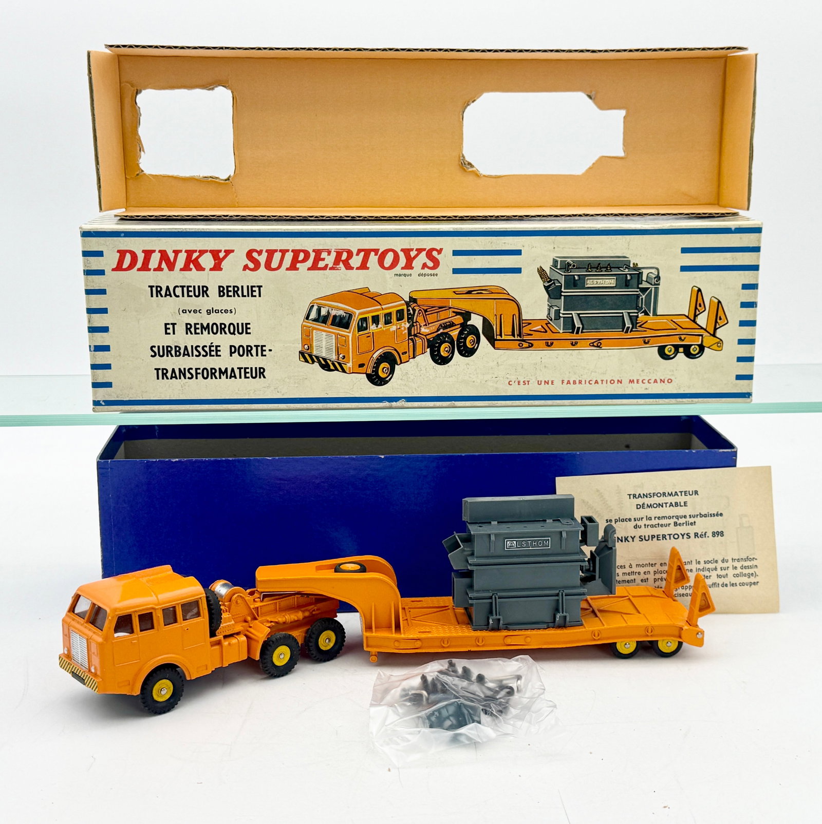 French Dinky Supertoys 898 Berliet Low Loader with Transformer: A French Dinky Supertoys 898 set featuring a die-cast orange Berliet tractor and low-loader trailer. The lot includes a gray Alsthom transformer load, original instruction sheet, and a bag of black pl