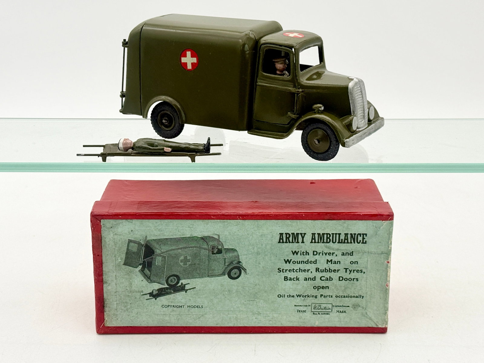 Britains No. 1512 Army Ambulance with Driver and Wounded Man: W. Britain Model No. 1512 Army Ambulance set featuring a die-cast metal vehicle finished in olive drab paint. The vehicle includes functional opening cab and rear doors, black rubber tires, and red cr