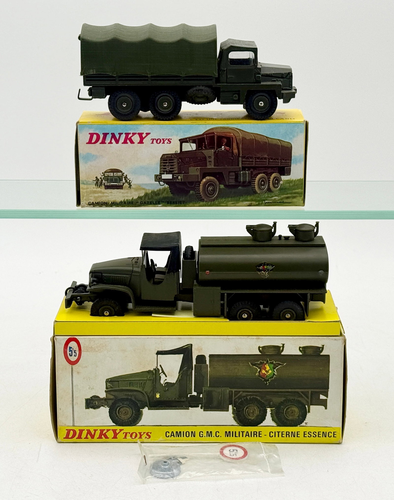 A Pair of French Dinky Toys Military Vehicles with Boxes: This lot features two French Dinky Toys die-cast military vehicles, including a G.M.C. tanker and a Berliet Gazelle truck. Each model is finished in olive drab paint and accompanied by its original il
