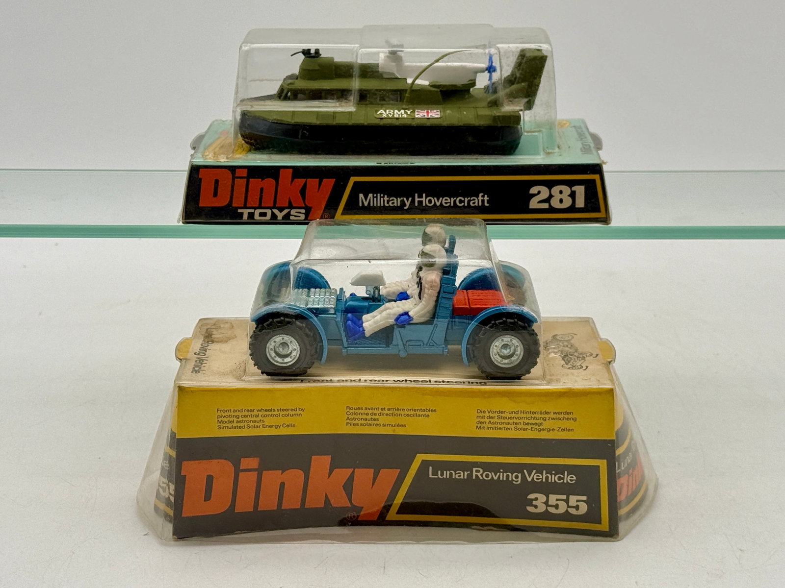 Two Vintage Dinky Toys Die-Cast Vehicles in Original Bubble Packaging: Dinky Toys die-cast models including a Military Hovercraft No. 281 and a Lunar Roving Vehicle No. 355. The hovercraft features an olive green finish with Army XV 814 and Union Jack decals, while the l