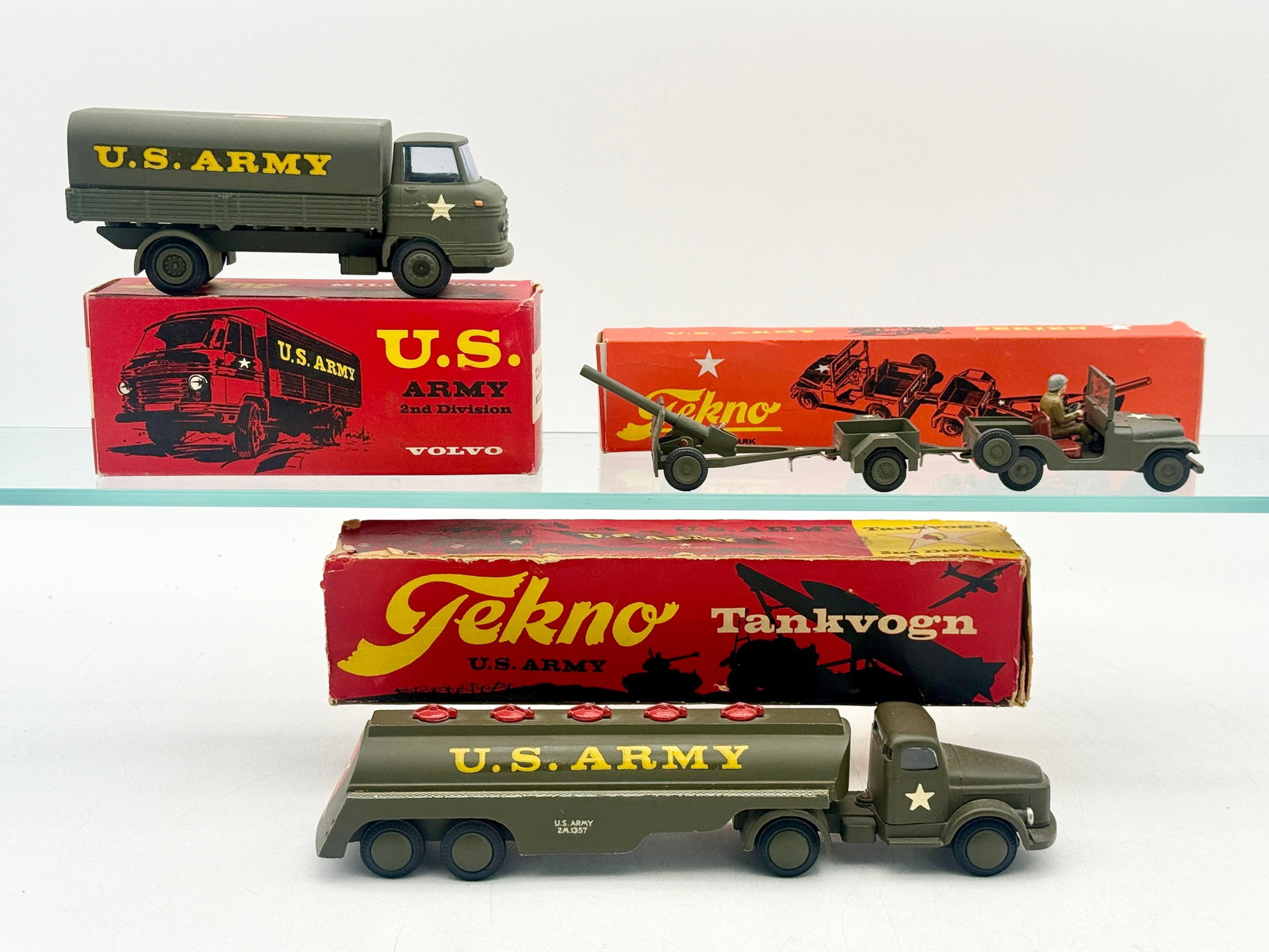A Group of Tekno Die-Cast U.S. Army Military Vehicles: This group of Tekno die-cast U.S. Army vehicles includes a Volvo truck, a fuel tanker, and a Jeep assembly. Construction consists of painted metal in olive drab with yellow stenciling and 2nd Infantry
