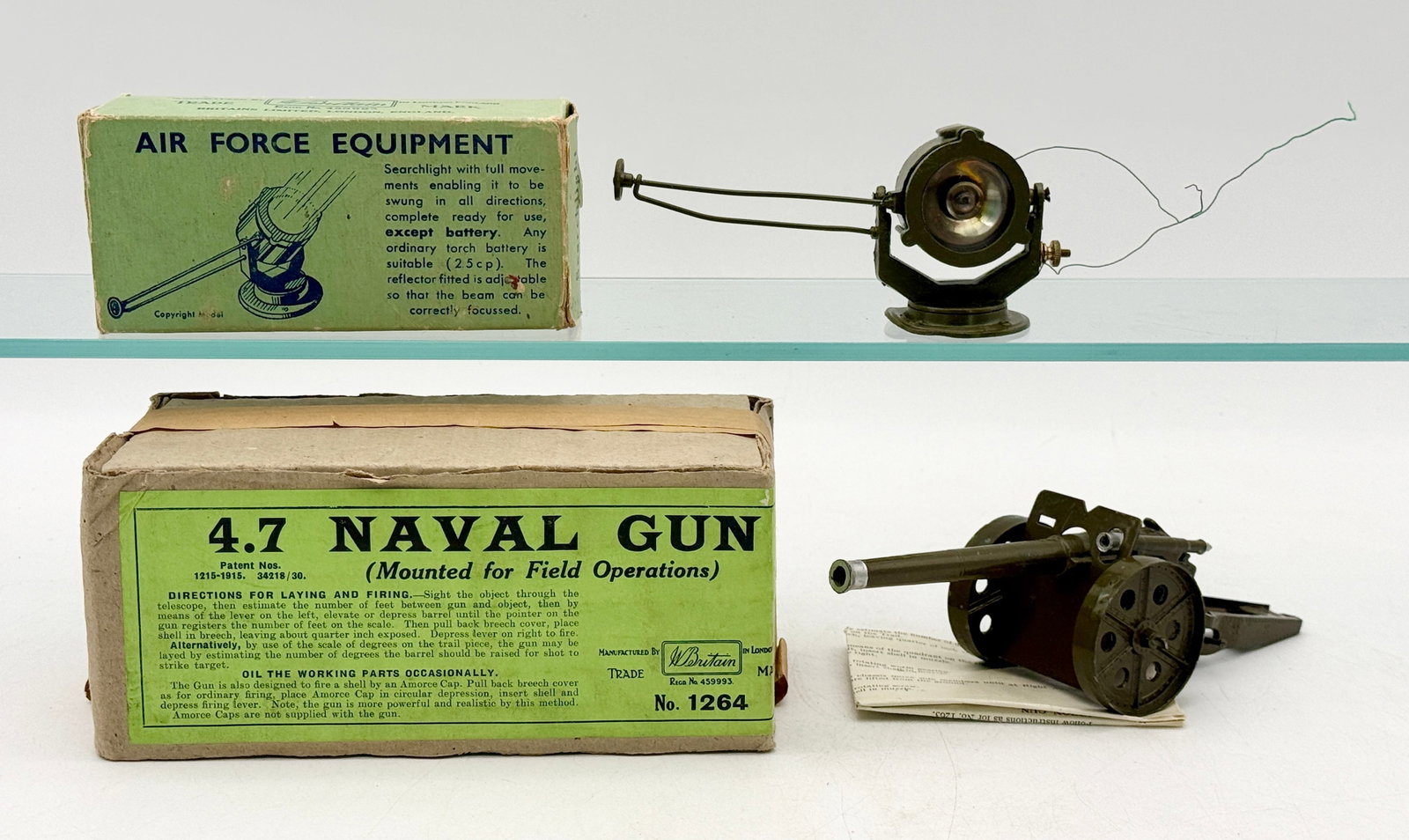 Two W. Britain Die-Cast Military Toys with Original Boxes: Manufactured by W. Britain, these two die-cast metal military toys include a No. 1264 4.7 Naval Gun and an Air Force Equipment searchlight. The naval gun features a green-painted body with black spoke