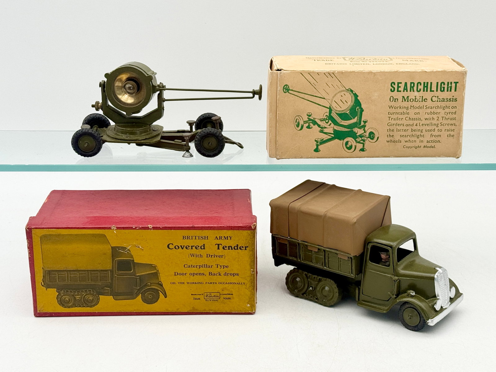 Two W. Britain Die-Cast Military Vehicles with Original Boxes: This W. Britain die-cast group includes a Searchlight on Mobile Chassis and a British Army Covered Tender. Each piece is constructed of die-cast metal with an olive green finish and features its respe