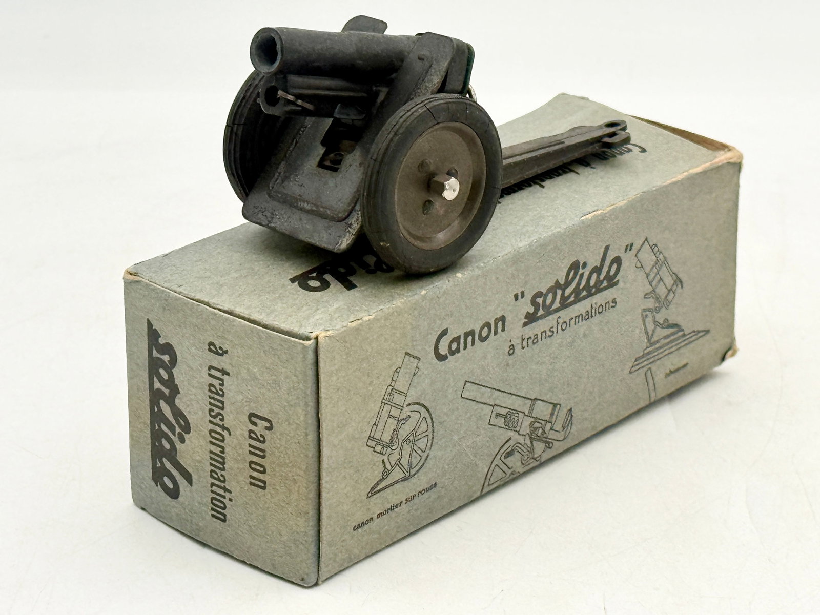 Solido Vintage Die-Cast Canon ? Transformations with Original Box: This Solido Canon à transformations toy features a die-cast metal artillery piece with a dark-patinated finish and adjustable components. The cannon is equipped with black rubber tires on metal