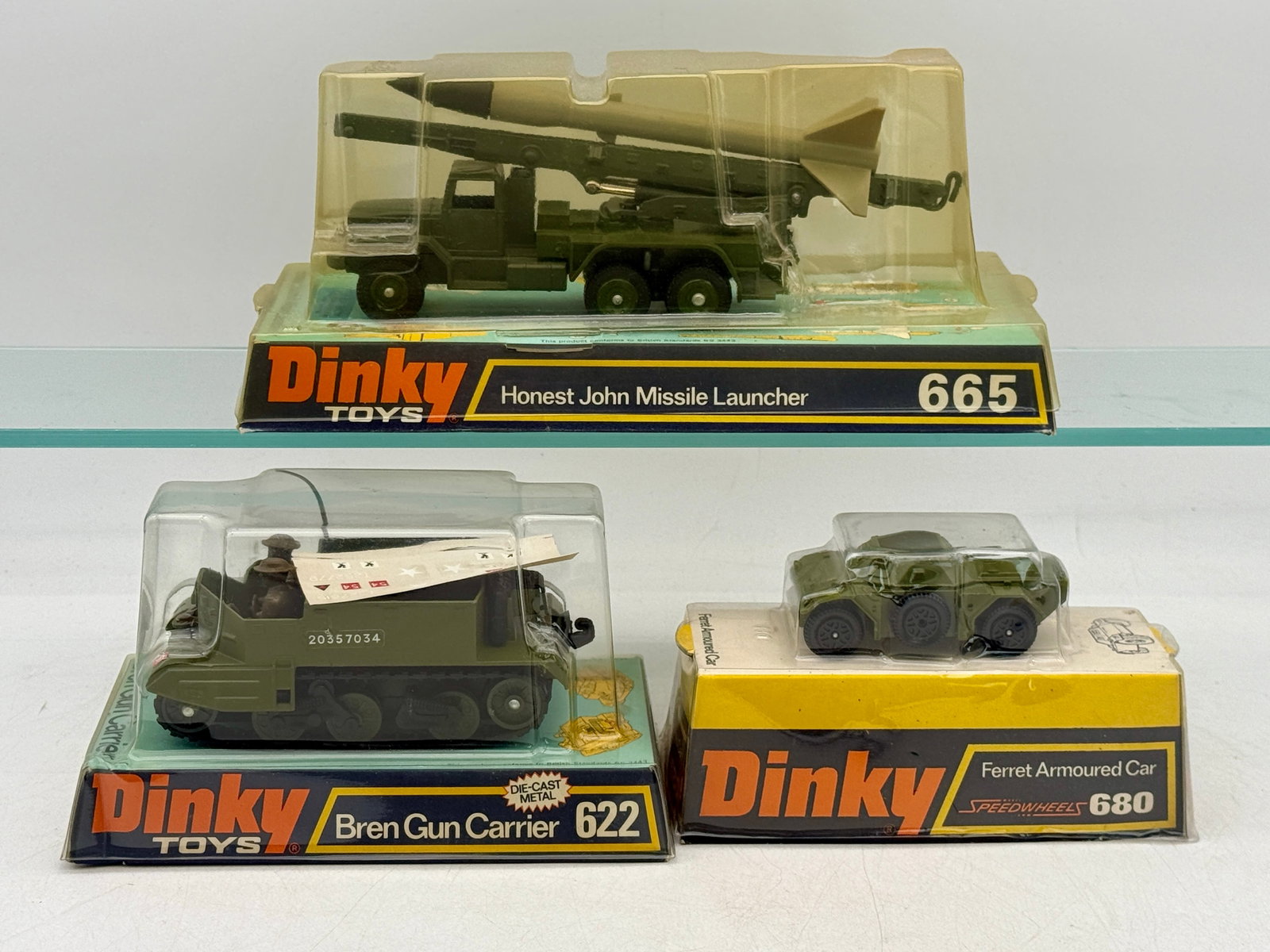 A Trio of Vintage Dinky Toys Die-Cast Military Vehicles: This Dinky Toys trio includes an Honest John Missile Launcher (665), a Bren Gun Carrier (622), and a Ferret Armored Car (680). The models are composed of die-cast metal finished in military olive drab