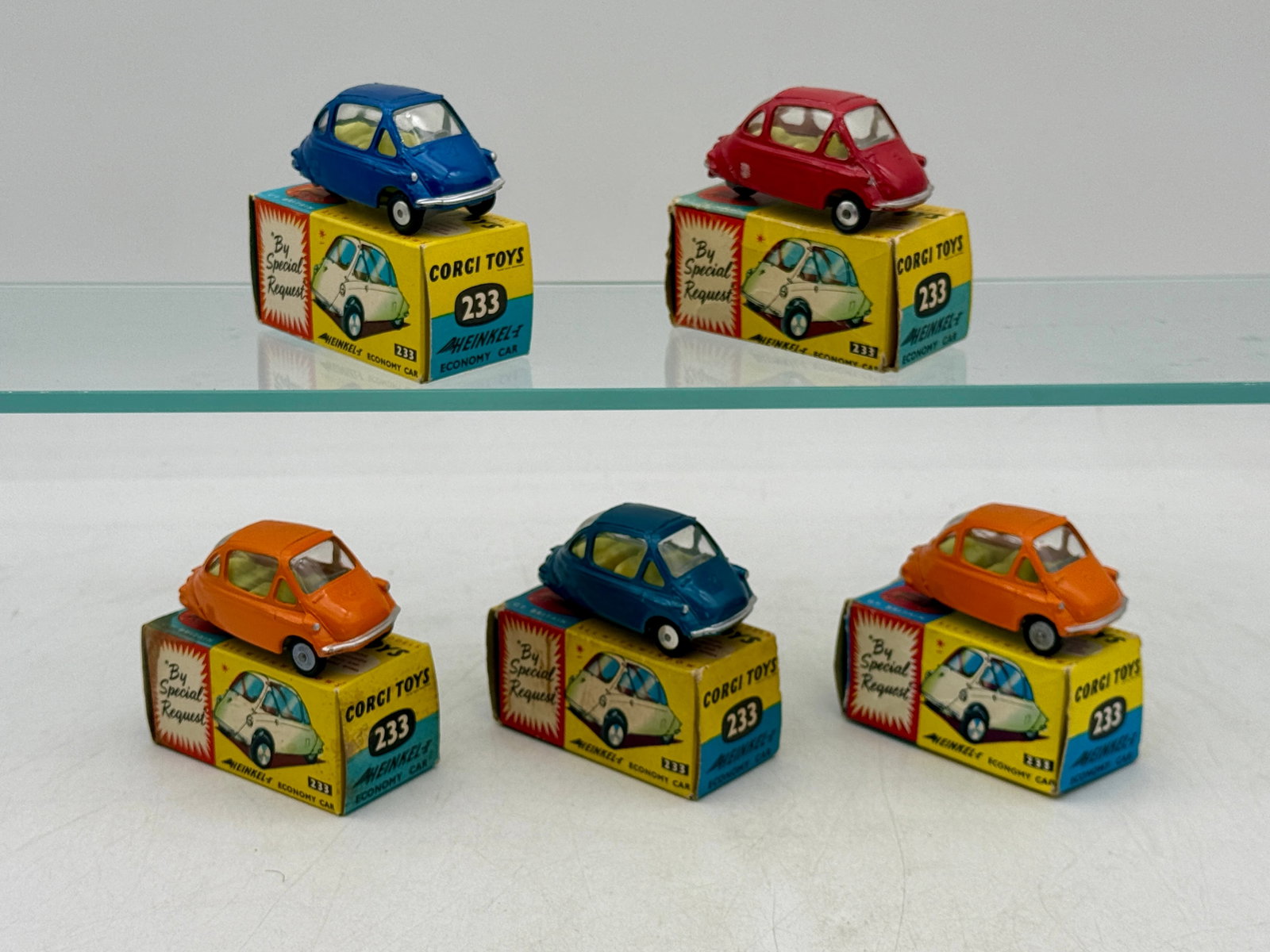A Collection of Corgi Toys No. 233 Heinkel Economy Cars: This collection features Corgi Toys No. 233 Heinkel Economy Cars in red, orange, and blue finishes. Each die-cast model includes molded interiors and transparent glazing, accompanied by its original i