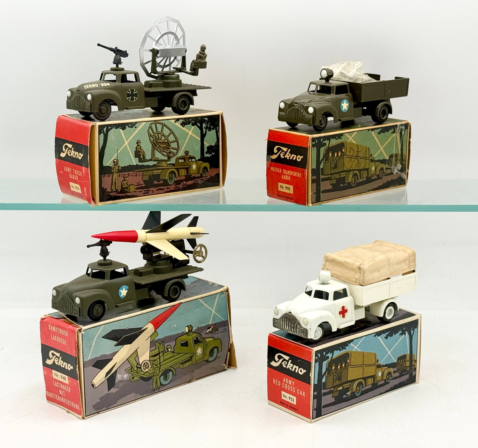 A Collection of Tekno Die-Cast Military Vehicles with Original Boxes: A collection of vintage Tekno die-cast military utility vehicles manufactured in Denmark. Each model is finished in either olive drab or white enamel and includes its original illustrated cardboard bo