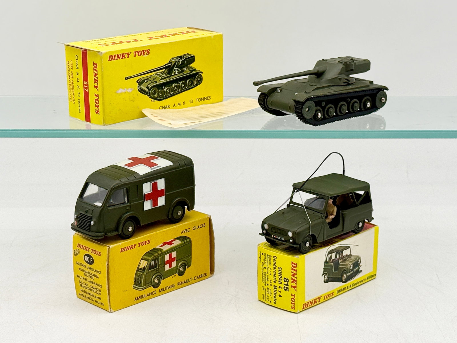Three French Dinky Toys Vintage Die-Cast Military Vehicles: Three French Dinky Toys die-cast military models: a Char A.M.X. 13 Tonnes tank, a Renault Carrier Ambulance, and a Sinpar 4x4 Gendarmerie. Each vehicle is finished in matte olive drab and housed in it
