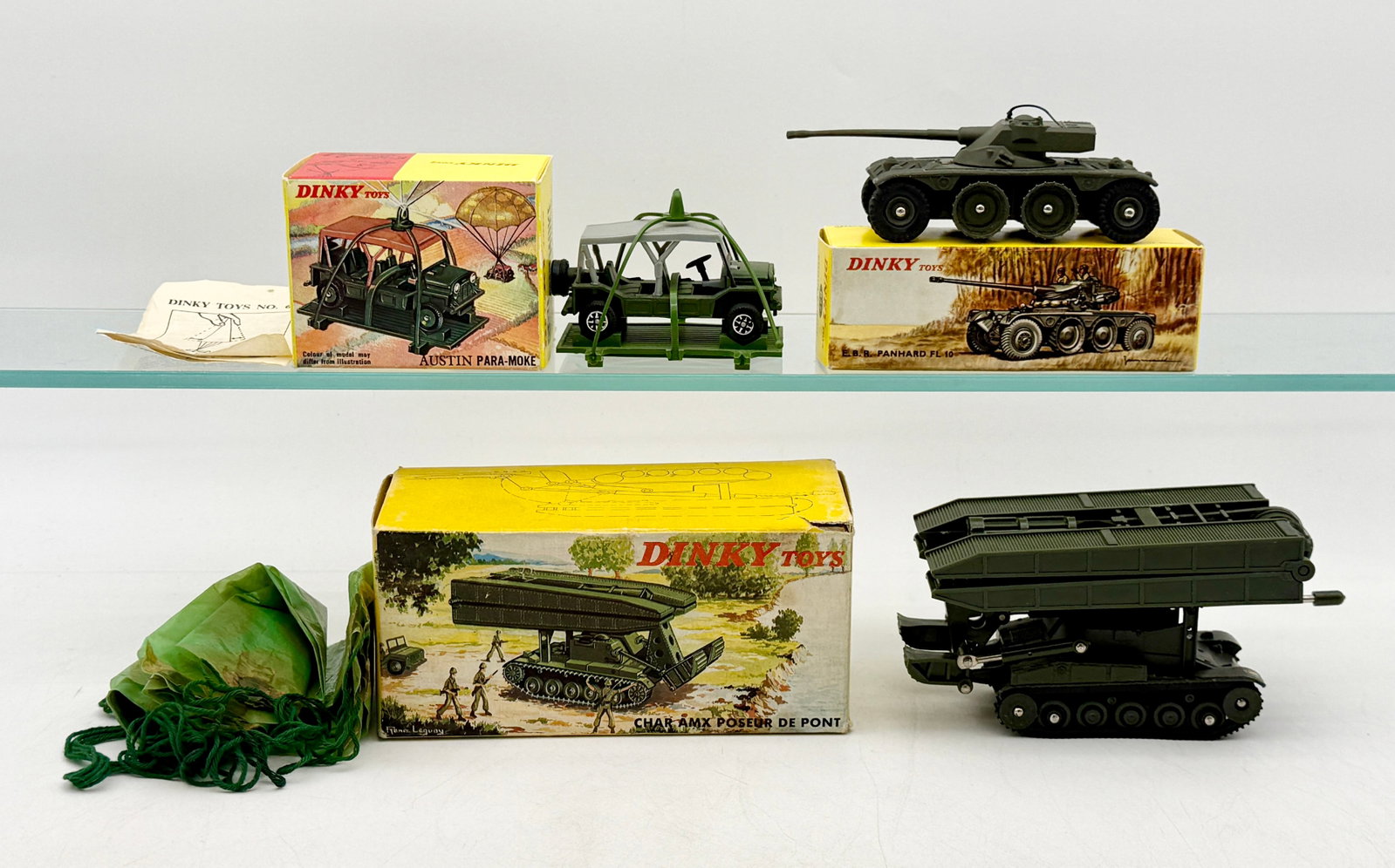 A Trio of Vintage Dinky Toys Military Vehicles with Boxes: This collection features three die-cast military models by Dinky Toys, including the No. 601 Austin Para-Moke, No. 827 Panhard E.B.R. armored car, and No. 883 Char AMX bridge-laying tank. Each vehicle
