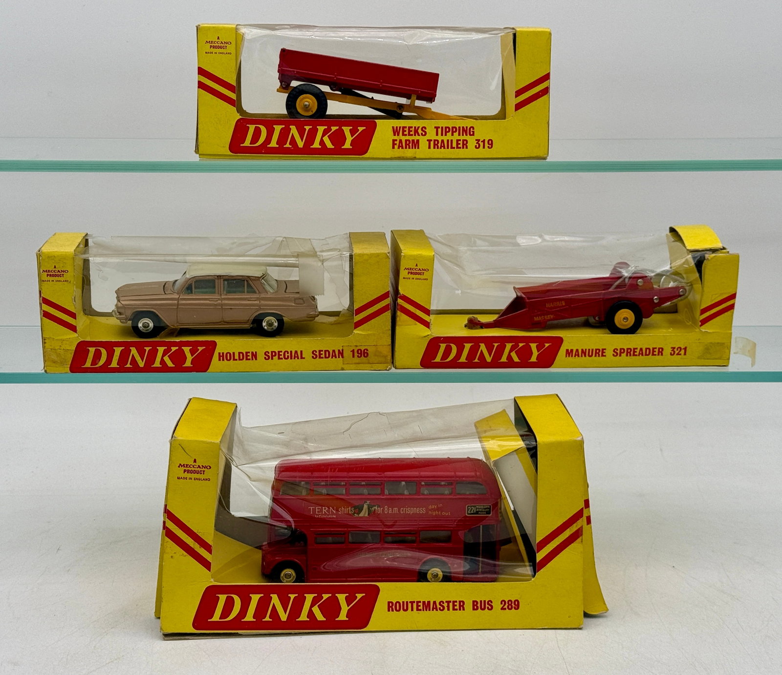A Group of Vintage Boxed Dinky Die-Cast Vehicles: A group of die-cast toy vehicles manufactured by Meccano in England, each housed in its original yellow and red window display packaging. The collection includes a Weeks Tipping Farm Trailer, a Holden