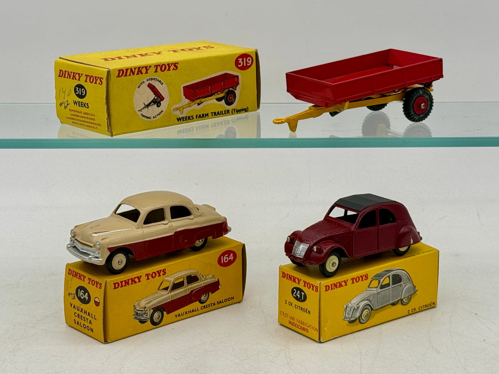 A Trio of Dinky Toys Die-Cast Vehicles with Boxes: Dinky Toys die-cast metal vehicles including a Weeks Farm Trailer, a Vauxhall Cresta Saloon, and a Citroen 2CV. Each vehicle is accompanied by its original yellow cardboard pictorial box displaying mo