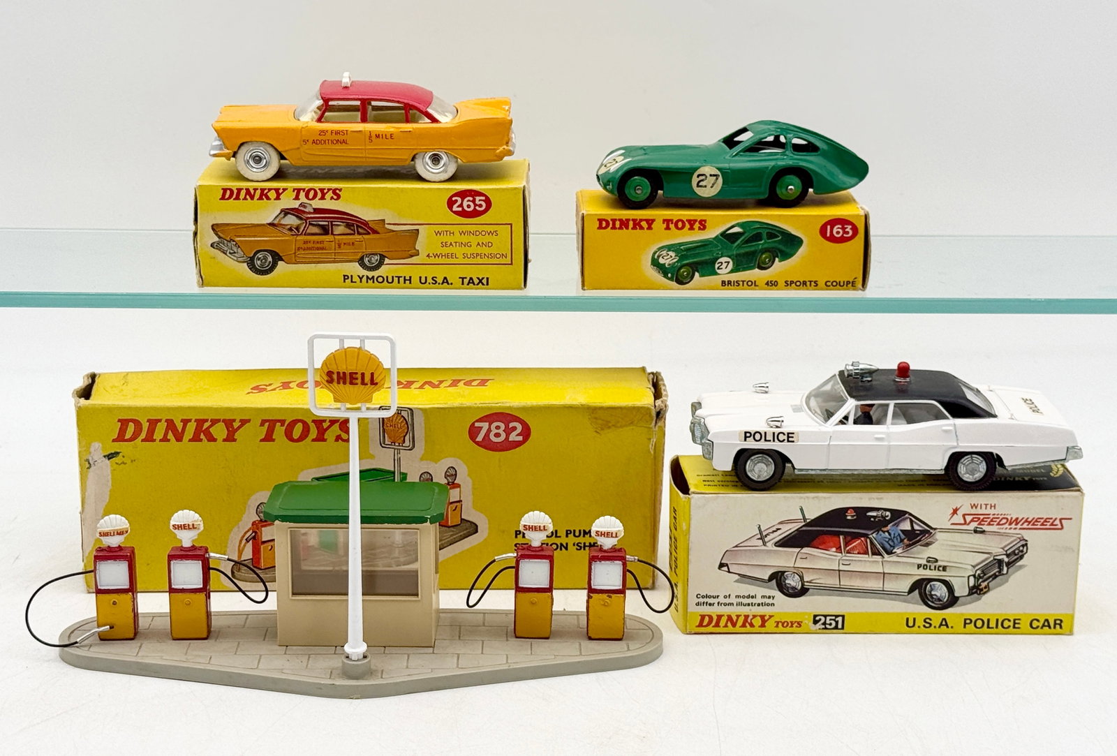 A Collection of Vintage Dinky Toys Vehicles and Accessories: A collection of Dinky Toys die-cast models including three vehicles and an accessory set. The lot features a No. 265 Plymouth U.S.A. Taxi, a No. 163 Bristol 450 Sports Coupé, a No. 251 U.S.A. P