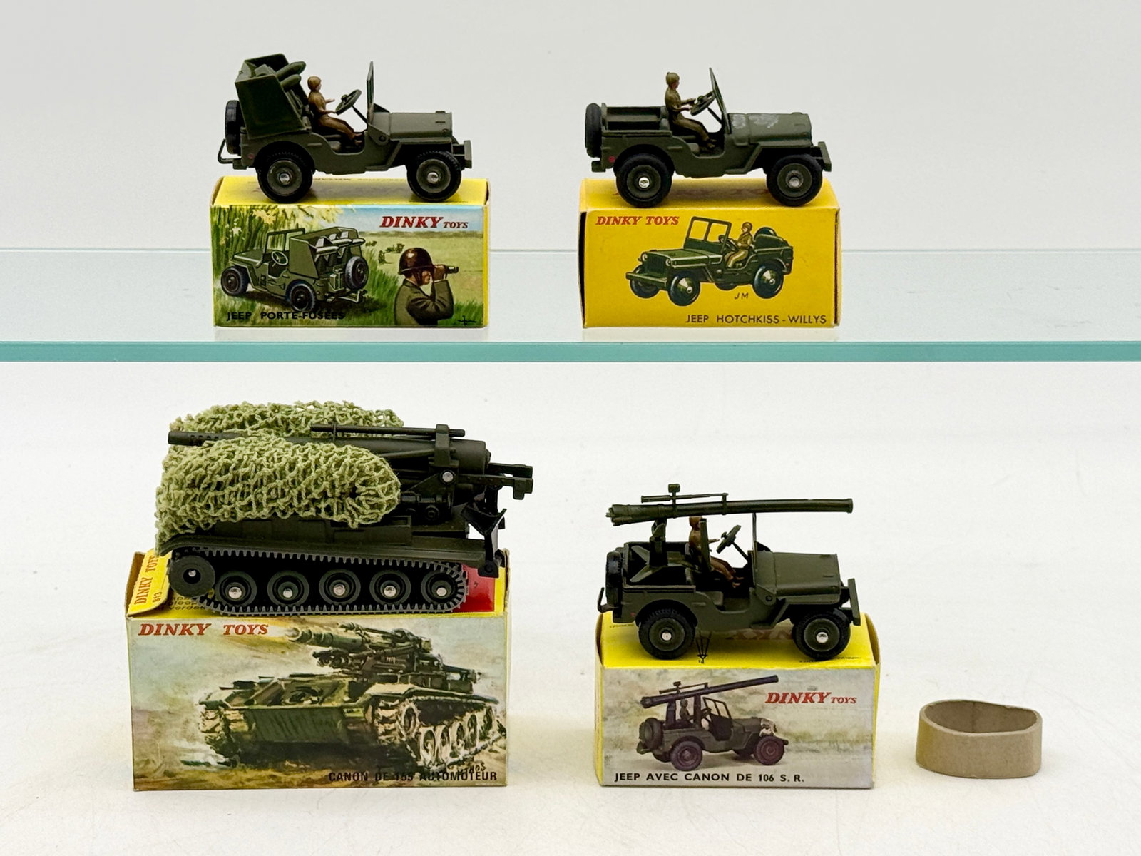 A Group of French Dinky Toys Military Die-Cast Vehicles: This group consists of French Dinky Toys military die-cast vehicles finished in olive drab with their original pictorial boxes. The collection features a 155mm self-propelled gun with camouflage netti