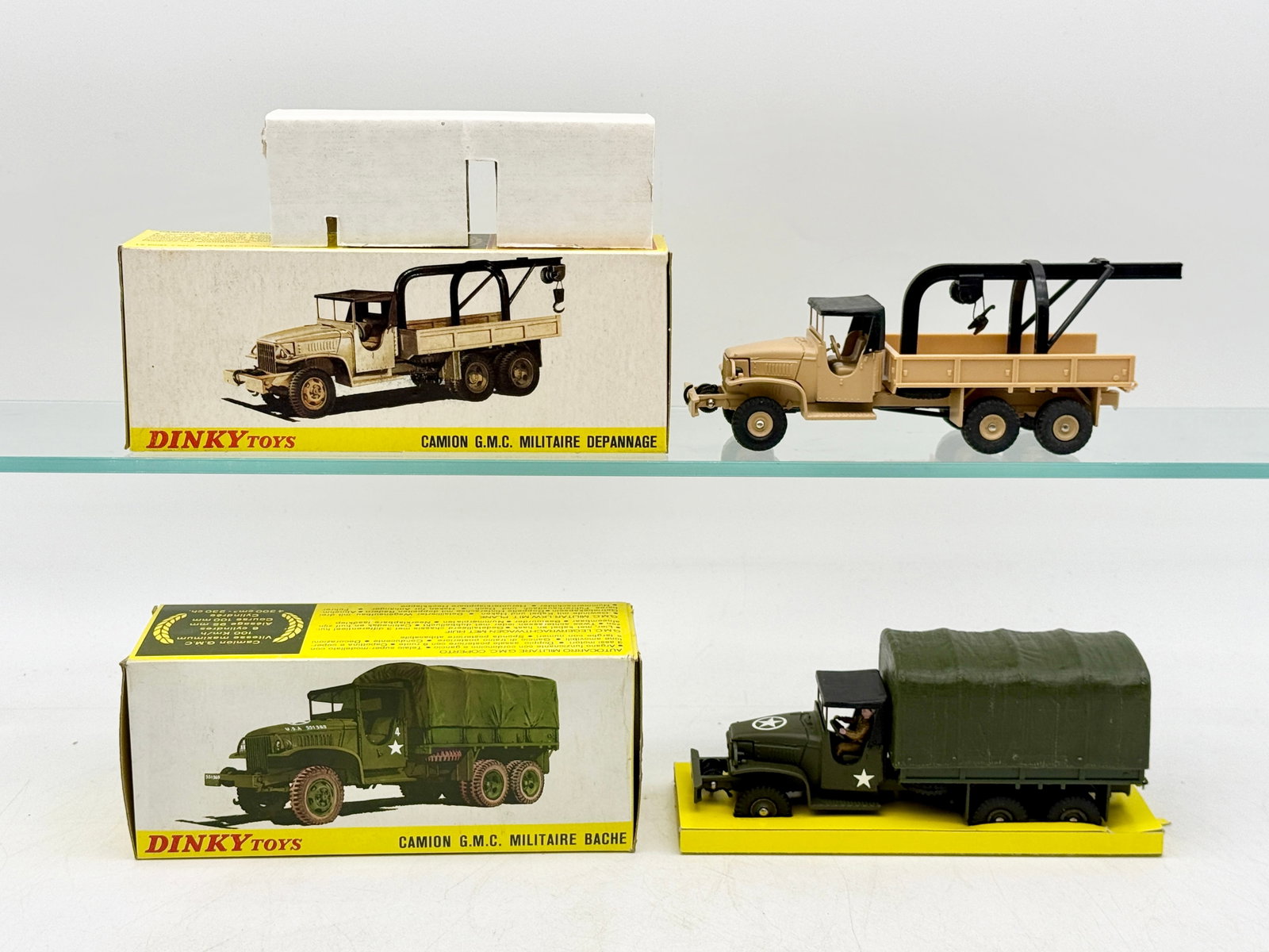 A Pair of French Dinky Toys Military GMC Trucks: Manufactured by Dinky Toys, this pair of die-cast metal military vehicles includes two GMC trucks in their original packaging. The collection features model 808, a recovery wrecker in tan, and model 8